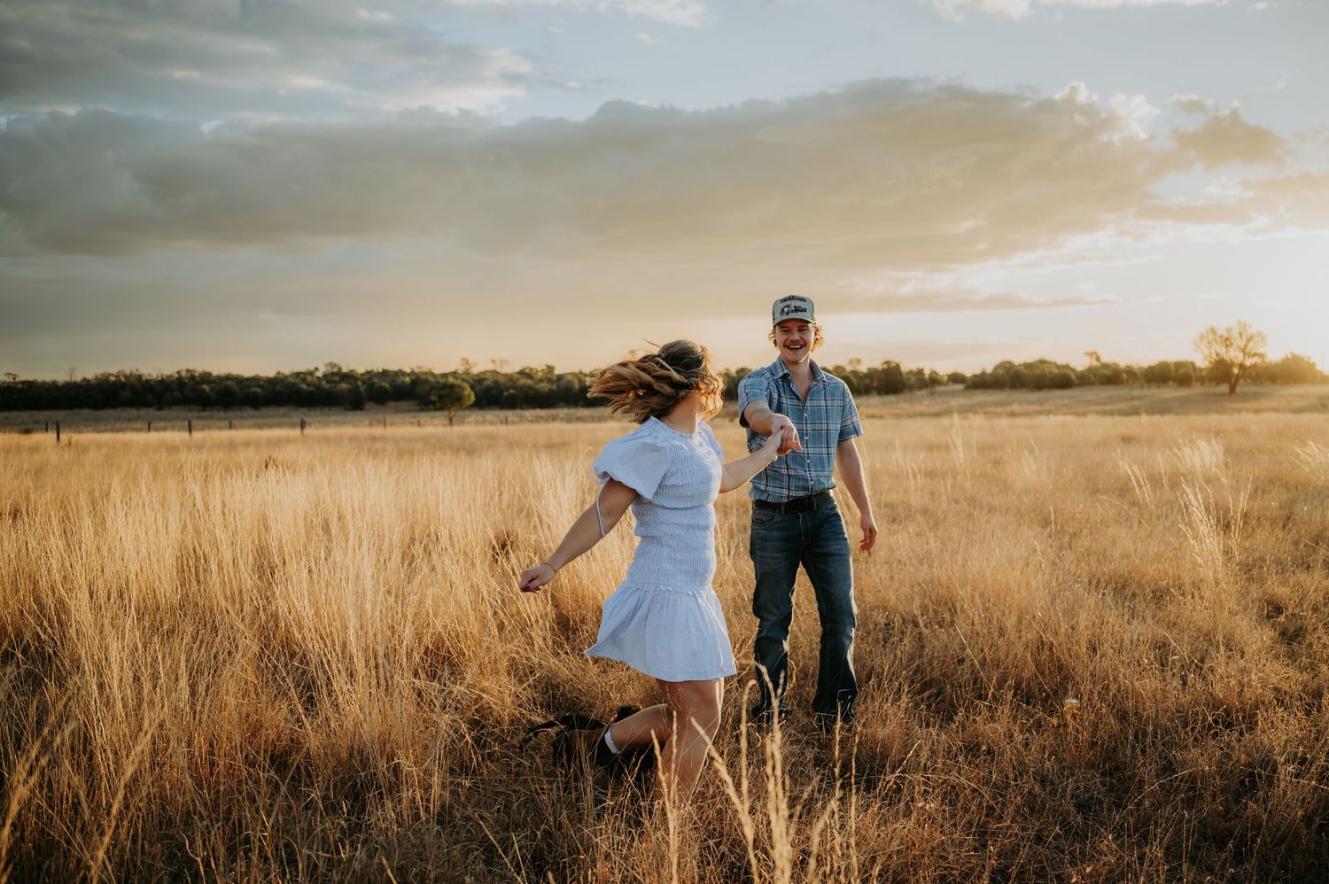 A woman in a white dress runs toward a man in a field of golden grass at sunset.