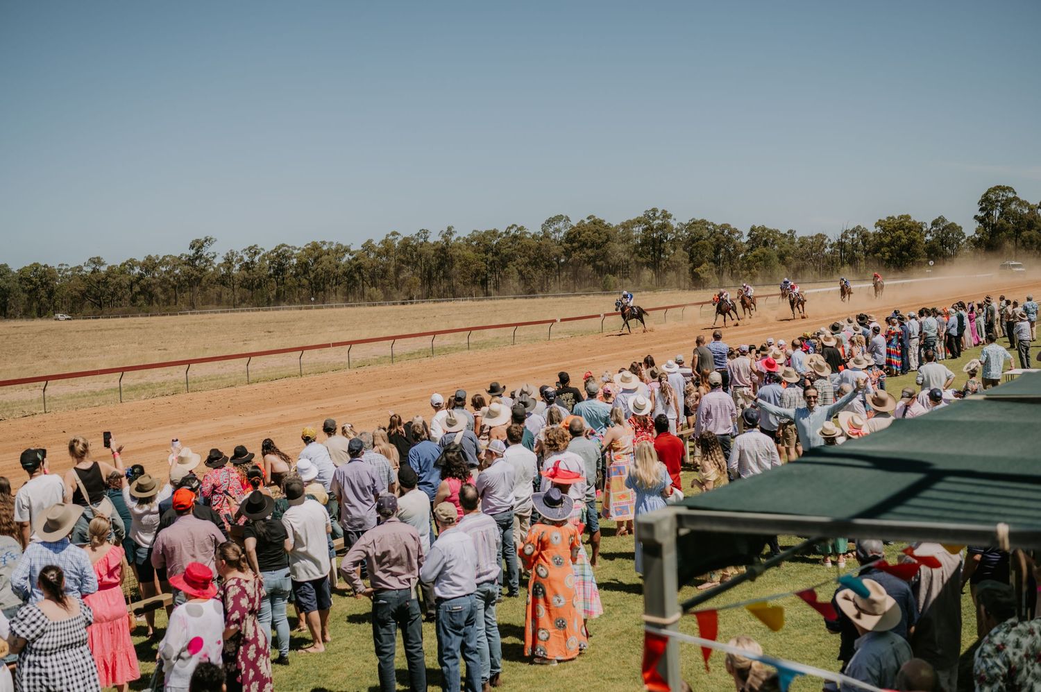 A panoramic view of a large outdoor crowd gathered at a rural event venue with tents and fencing.