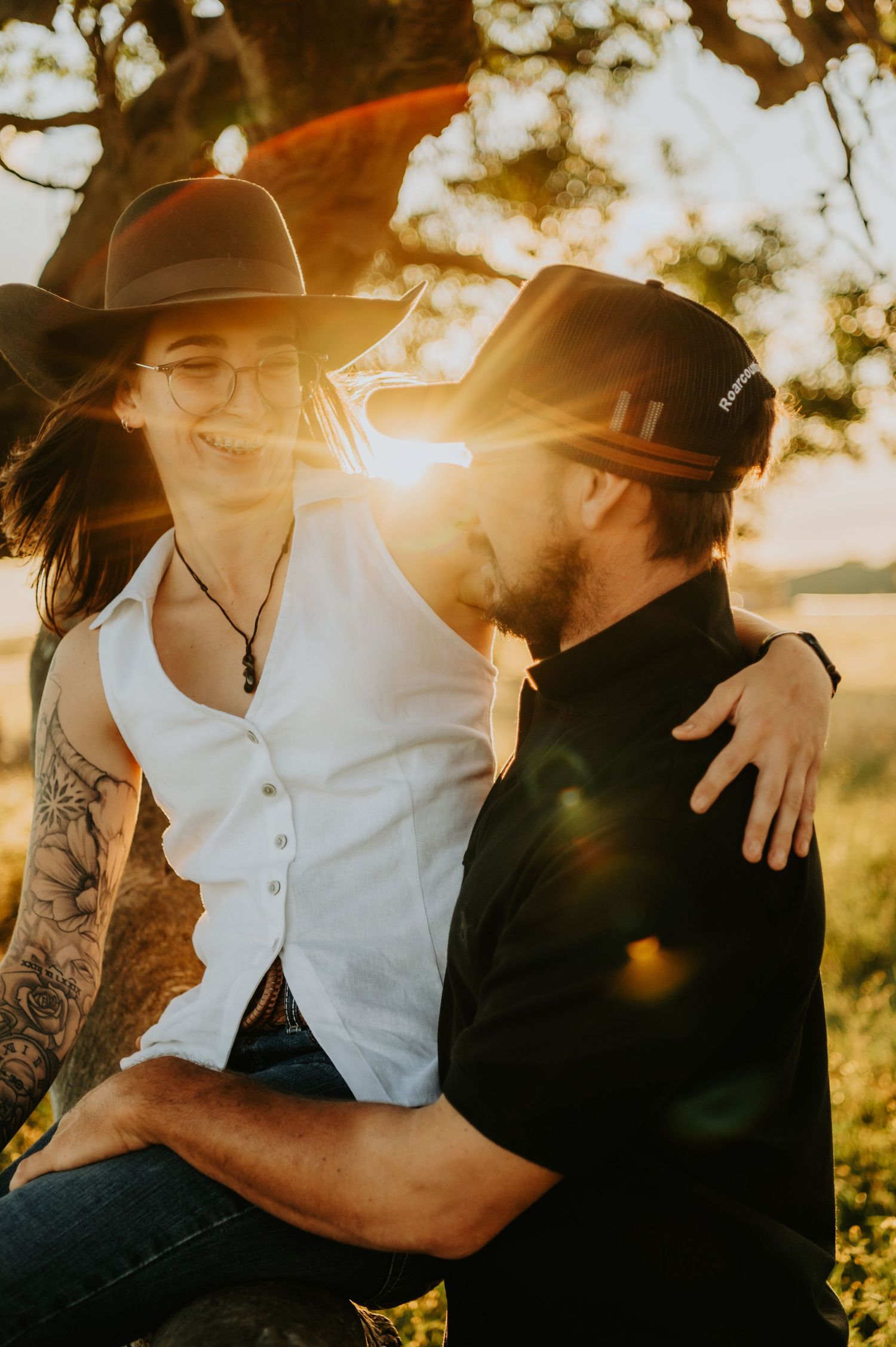 A couple in cowboy hats share an intimate moment at sunset with lens flare and natural lighting.
