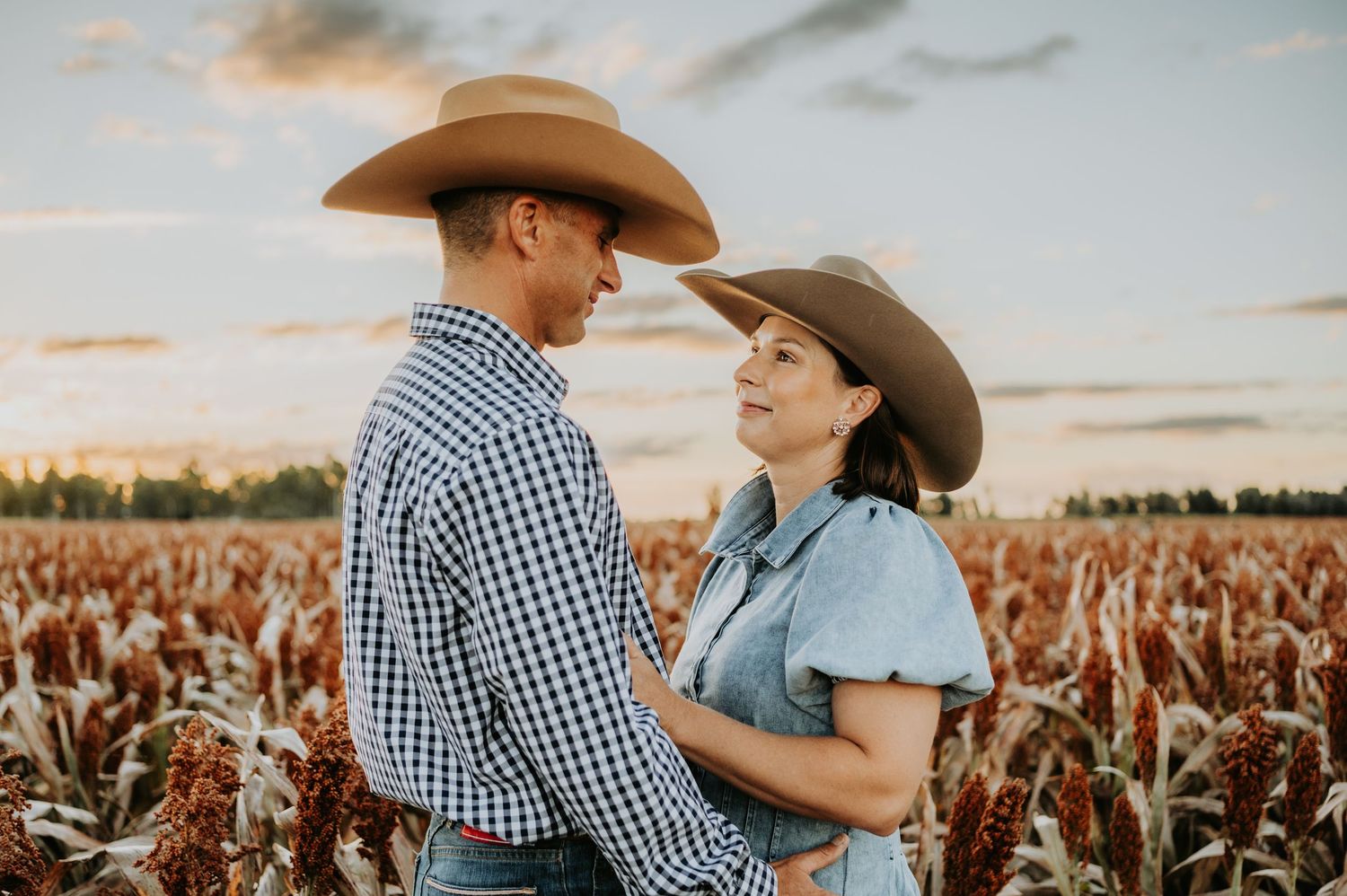 Couple in cowboy hats sharing a romantic moment in a sorghum field at sunset.