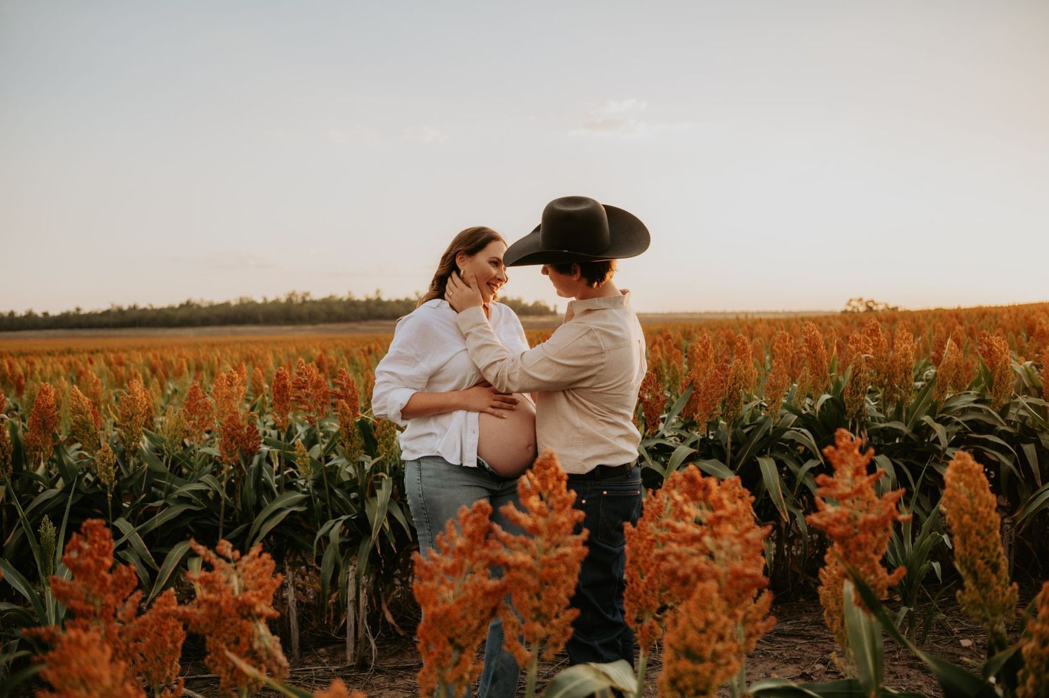 Couple sharing a tender moment in a golden sorghum field during a maternity photo shoot at sunset.