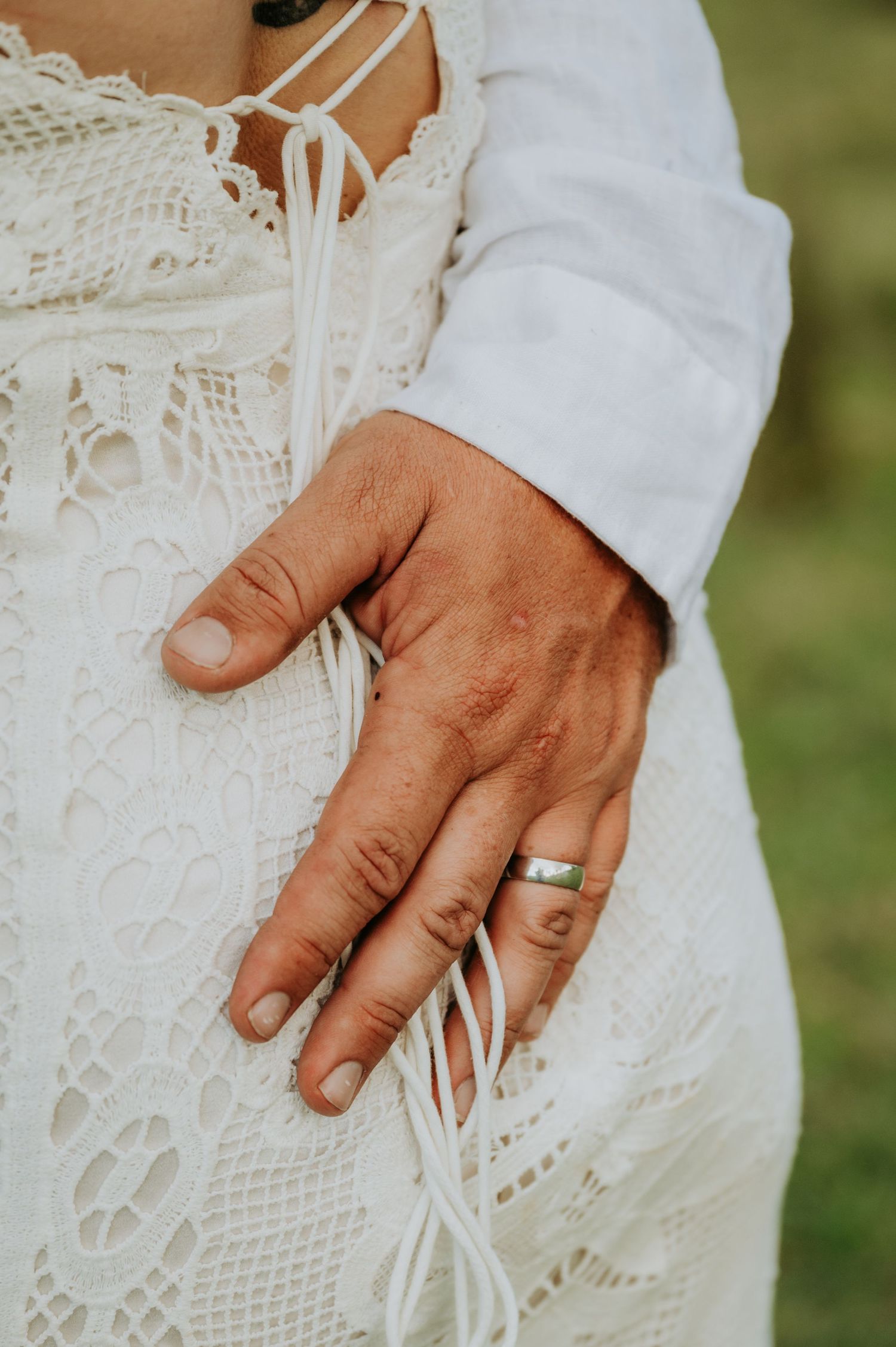 Close-up of a hand with a silver wedding band resting on a white lace wedding dress.