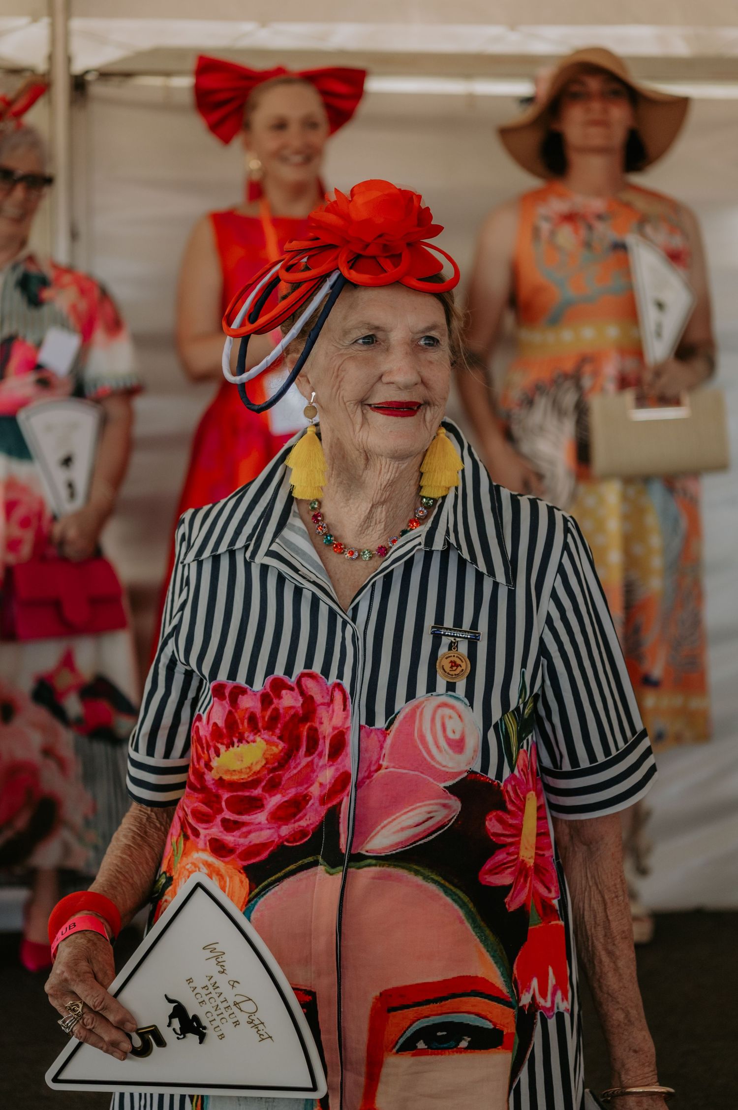 Ladies in colorful dresses and hats enjoying a festive outdoor social event.