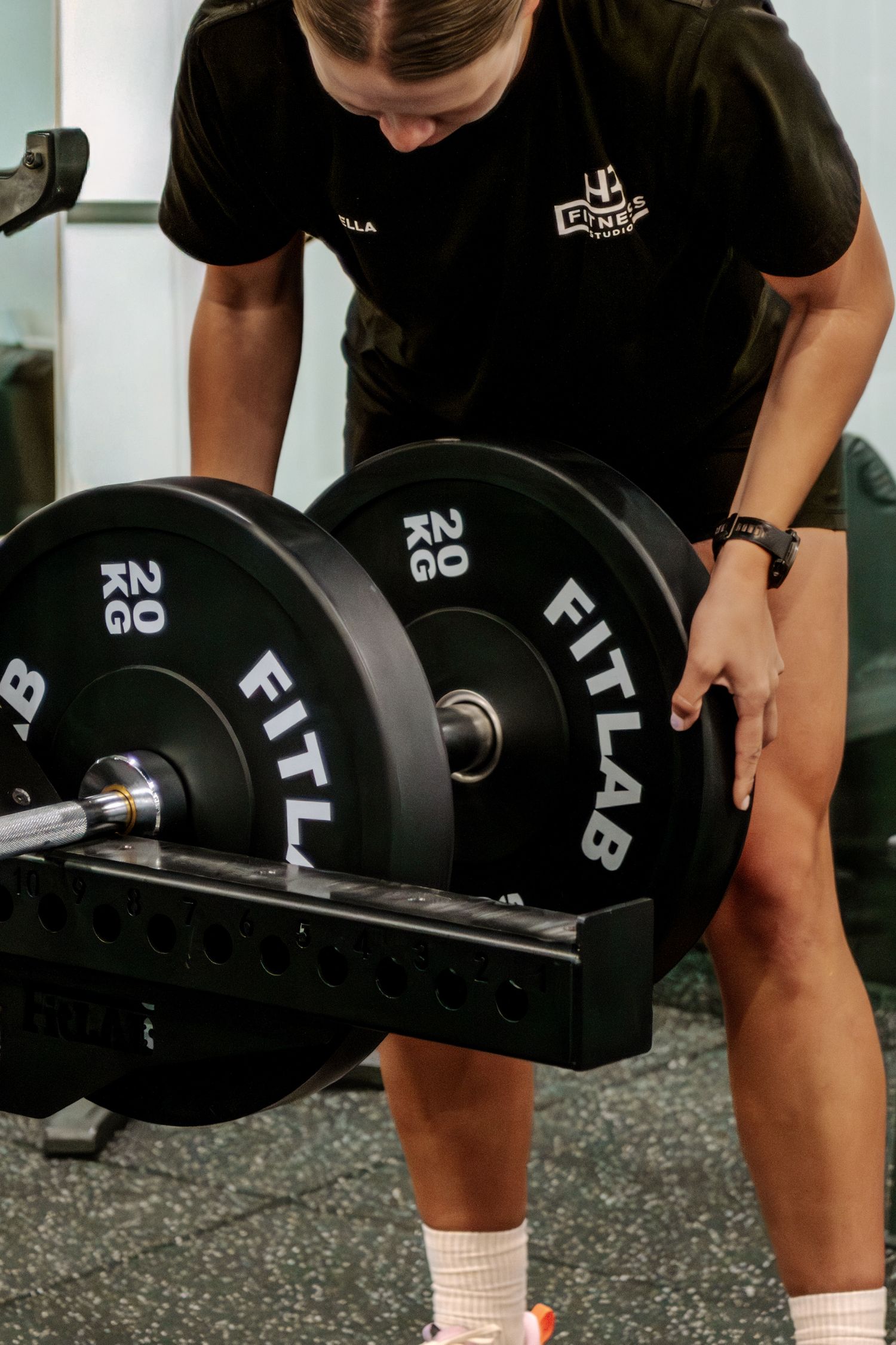 Woman loading 20kg FitLab bumper plates onto a barbell at a gym.