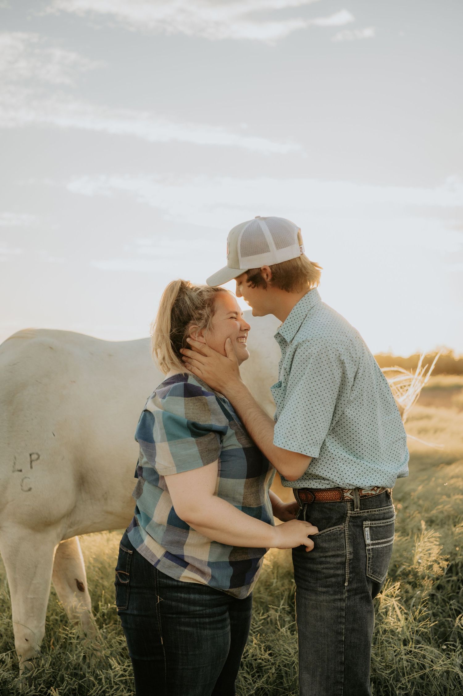 Couple sharing a romantic moment in a field with white horses at golden hour.