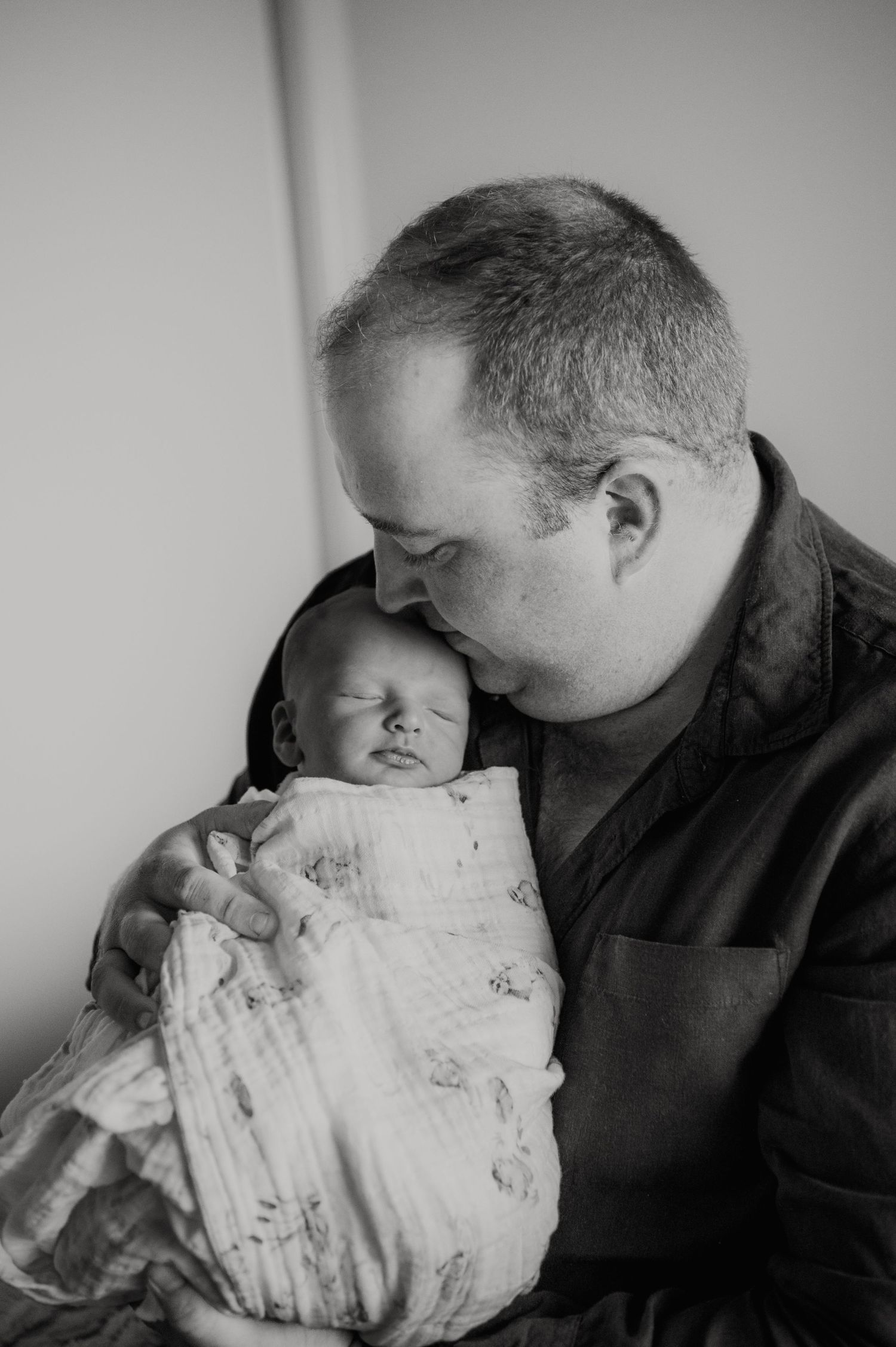 Black and white portrait of tender moment between adult and swaddled newborn.