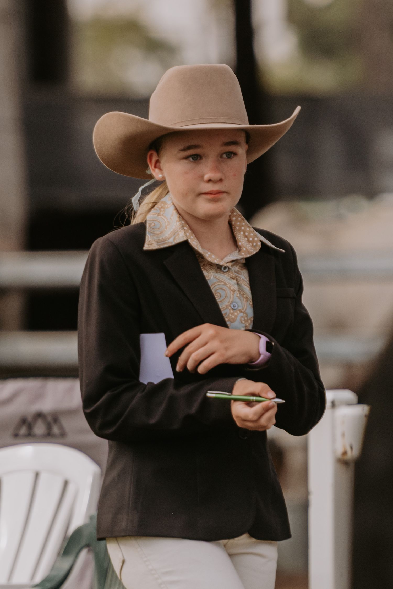 Young girl in tan cowboy hat and black blazer holding a pen and paper at an equestrian event.