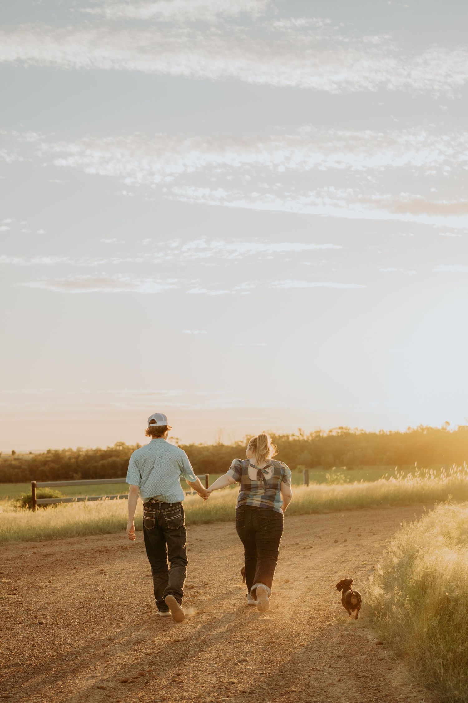Two people walk together on a country path with their dog during sunset.