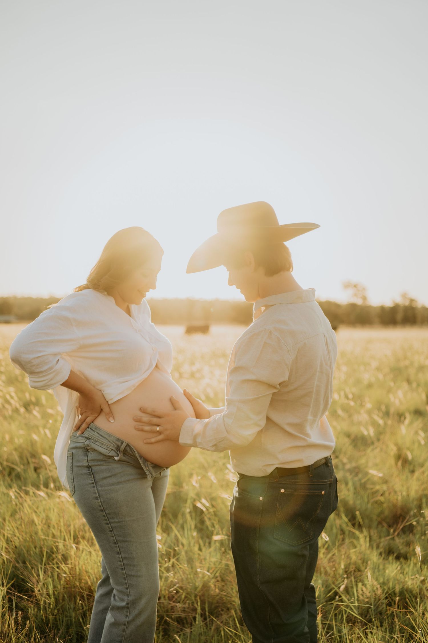 A maternity photo in golden sunlight with a rustic country setting.