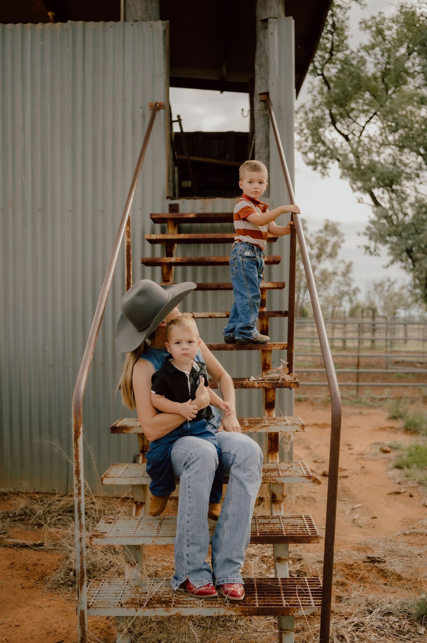 Children and adult sitting on metal stairs outside a rural building.