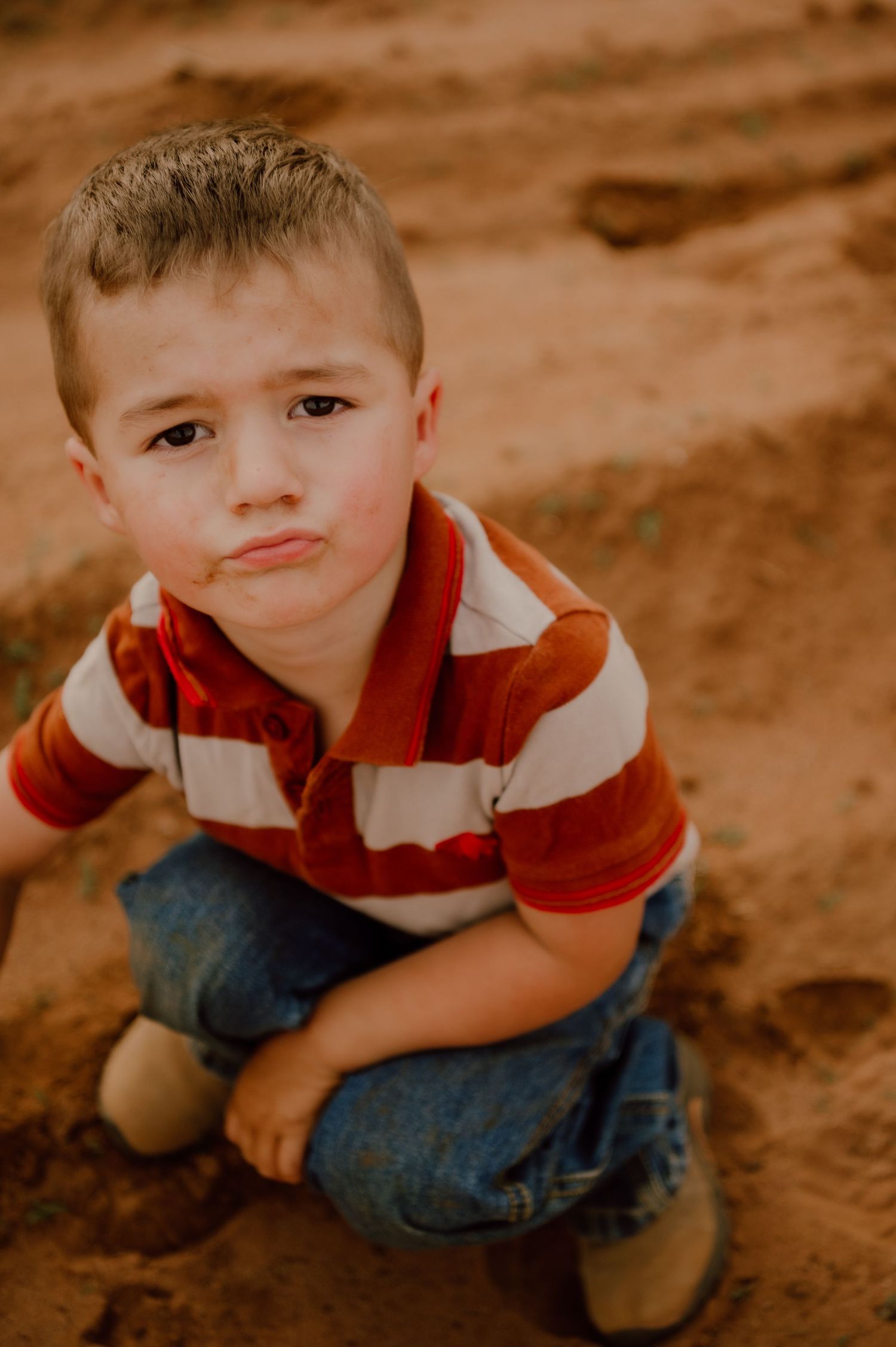 Close up shots of a young child in denim and red shirt crouching outdoors.