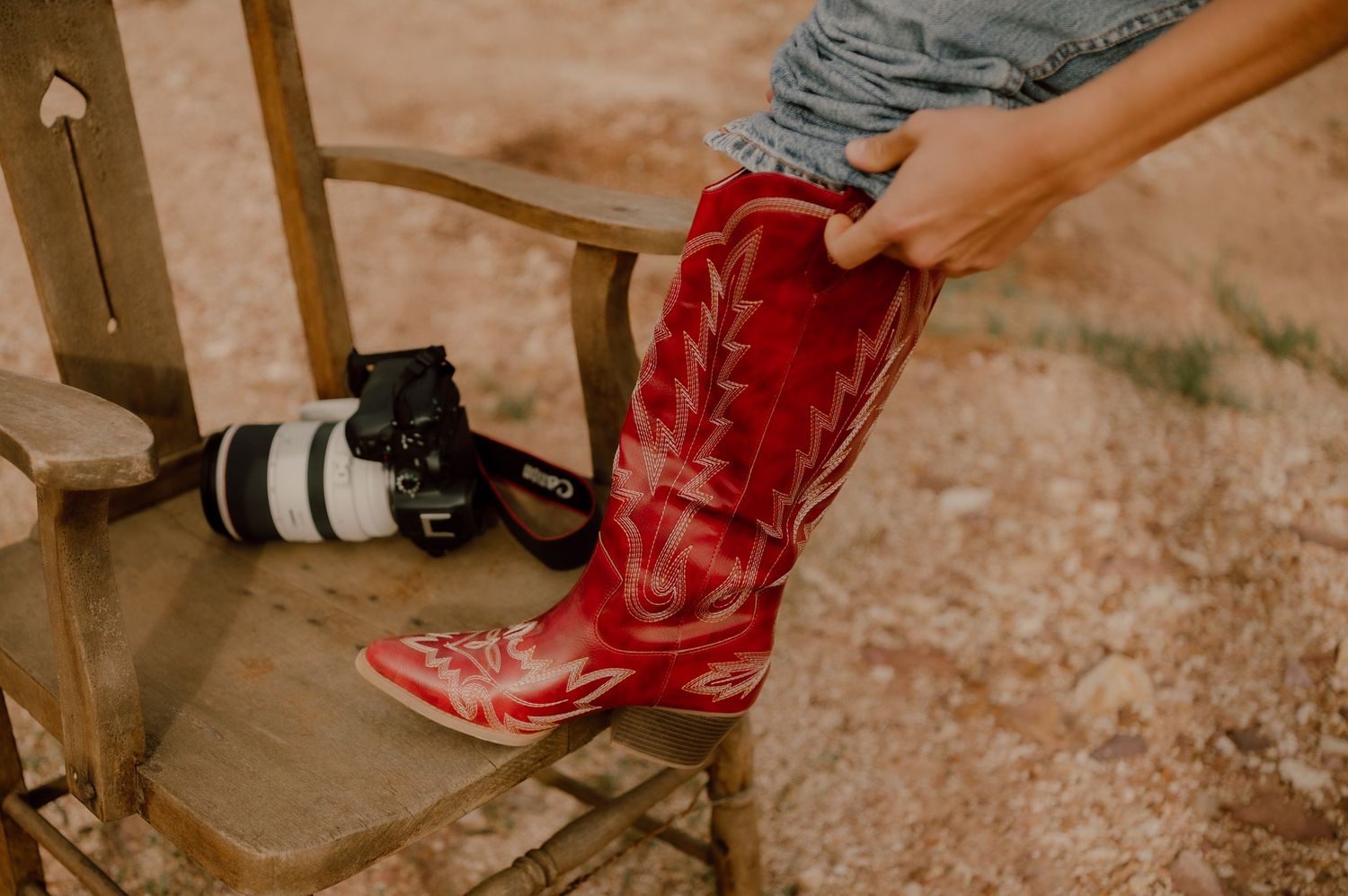 Red cowboy boots walking on dusty ground at a ranch.