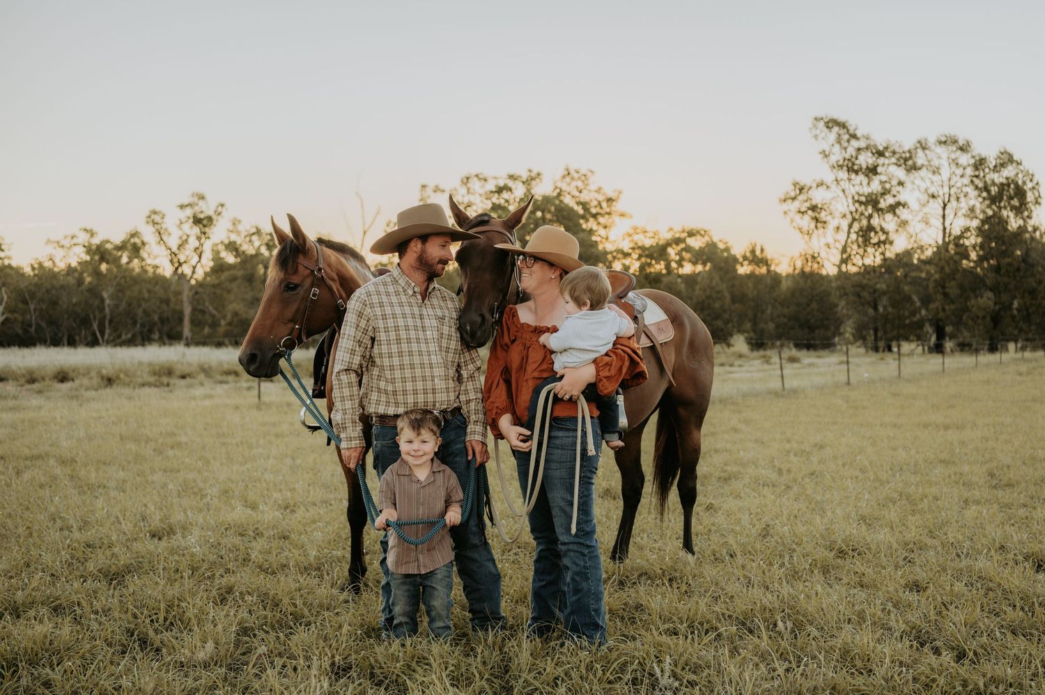 Group gathered in an open field during golden hour with horses visible in background.
