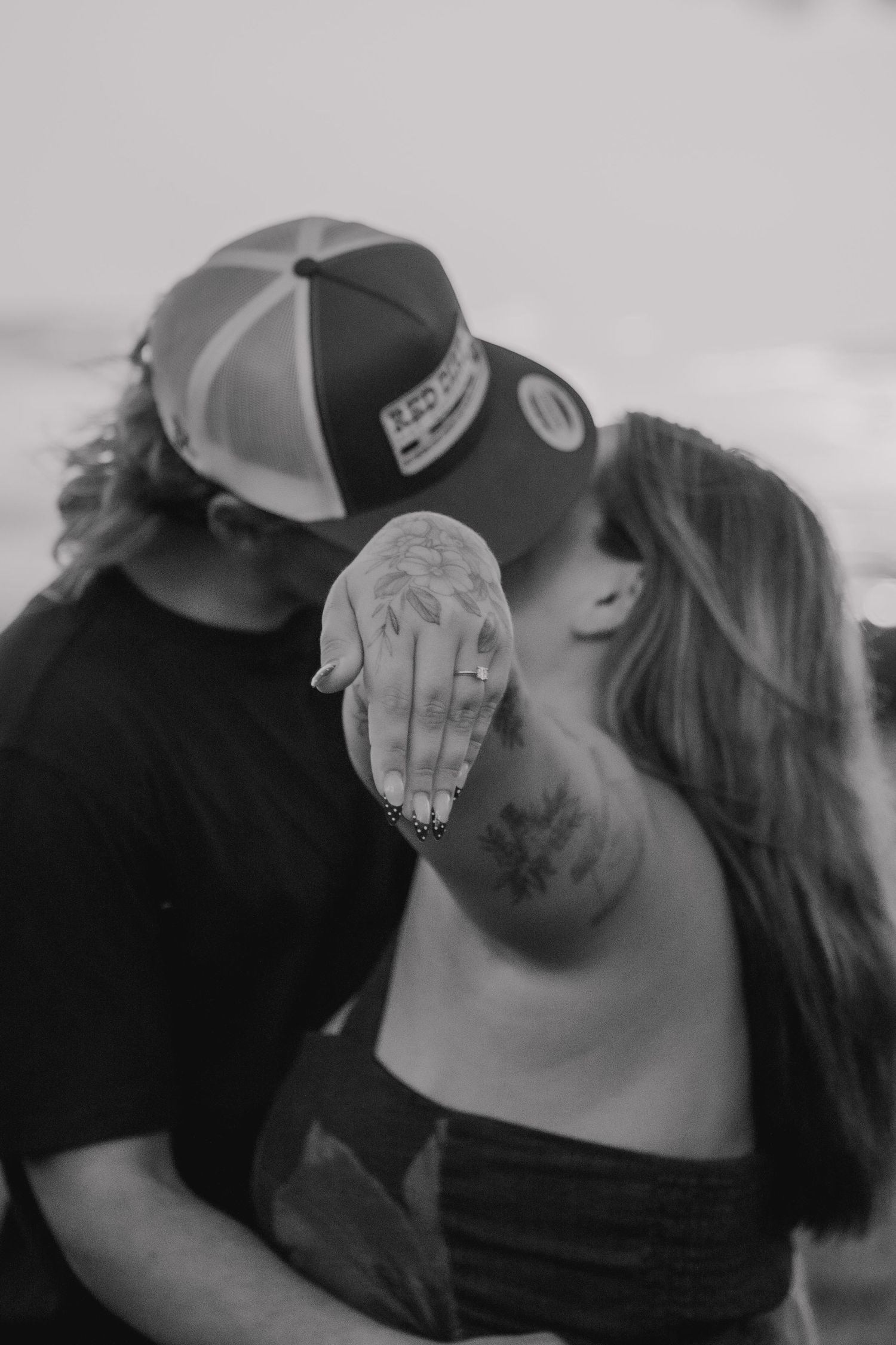 Black and white close-up of a couple sharing an intimate moment wearing baseball caps.