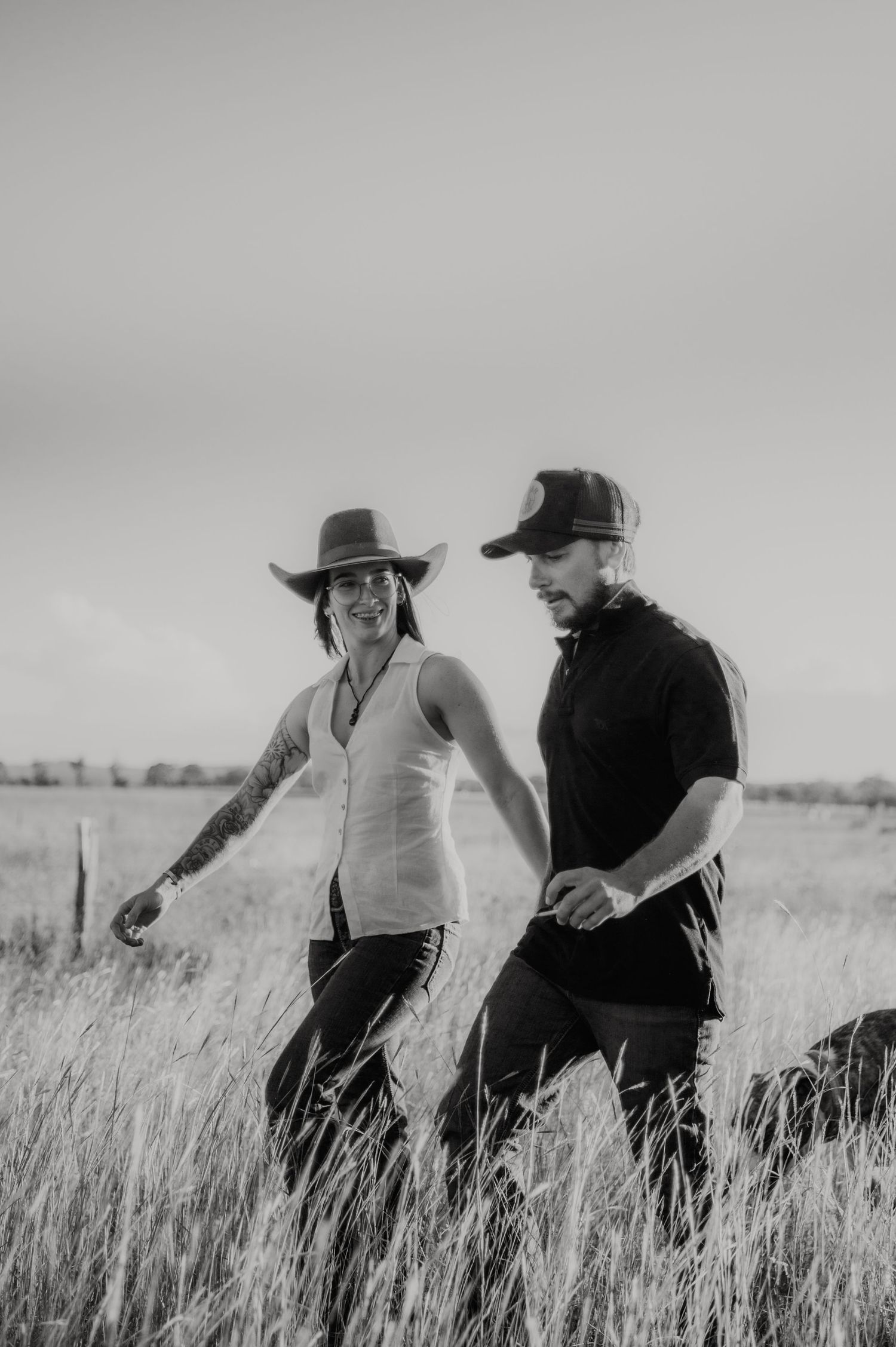 Two people in cowboy hats walk through a tall grass field in black and white photography.