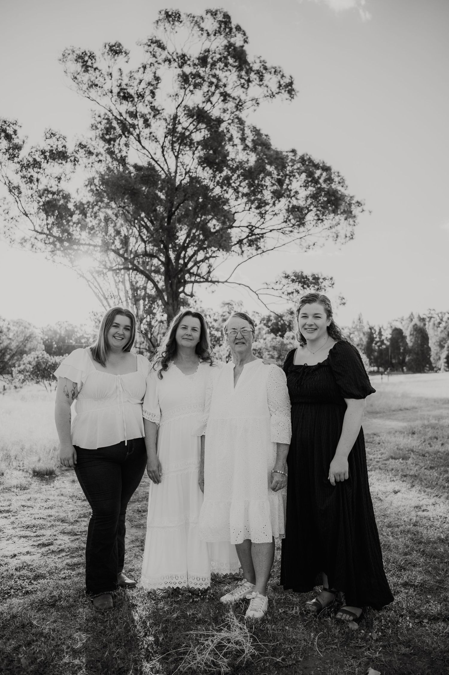 Black and white photo of four women smiling together outdoors near a large tree.