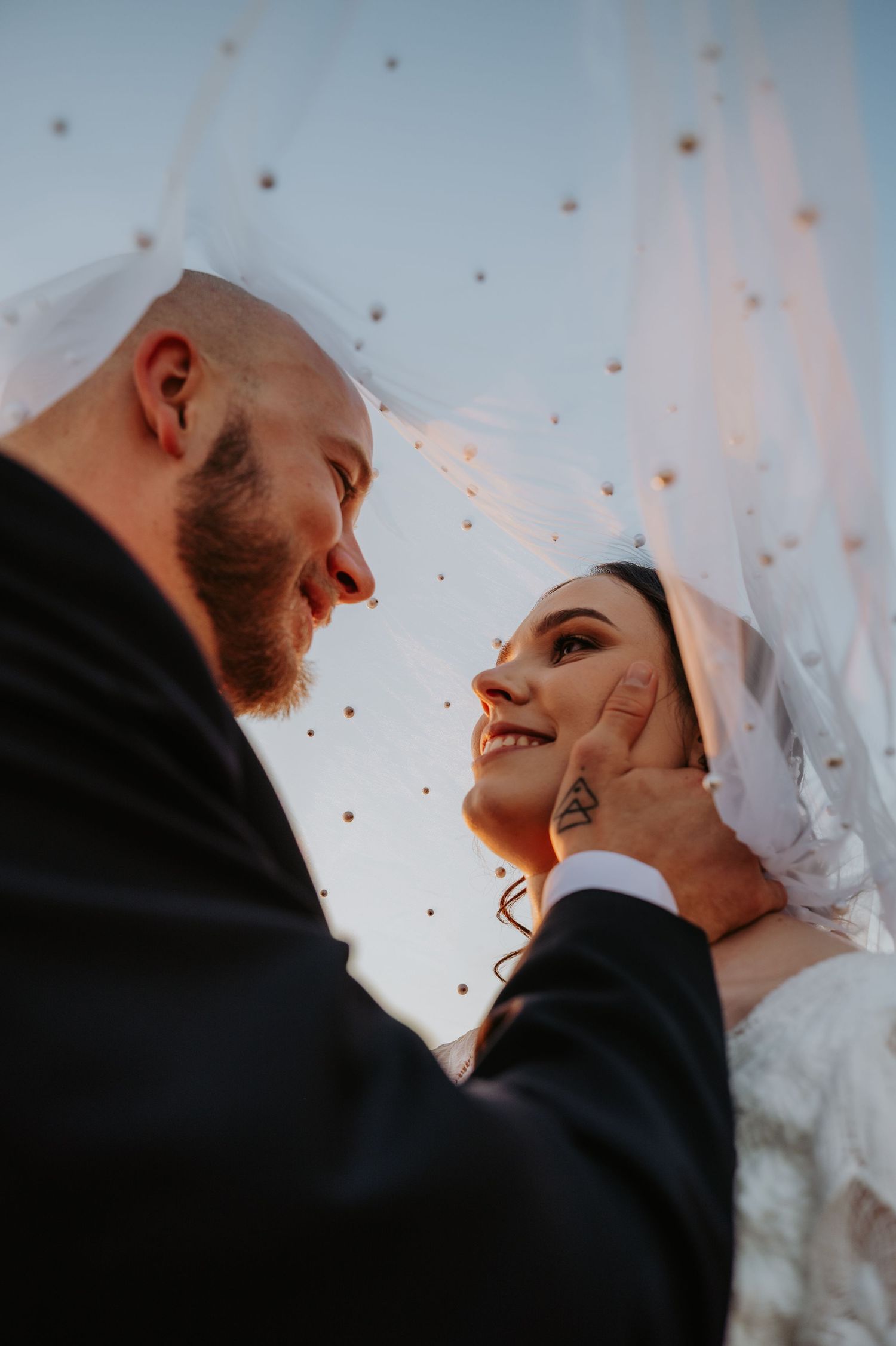 A groom tenderly cups his bride's face under her veil, sharing a romantic moment on their wedding day.