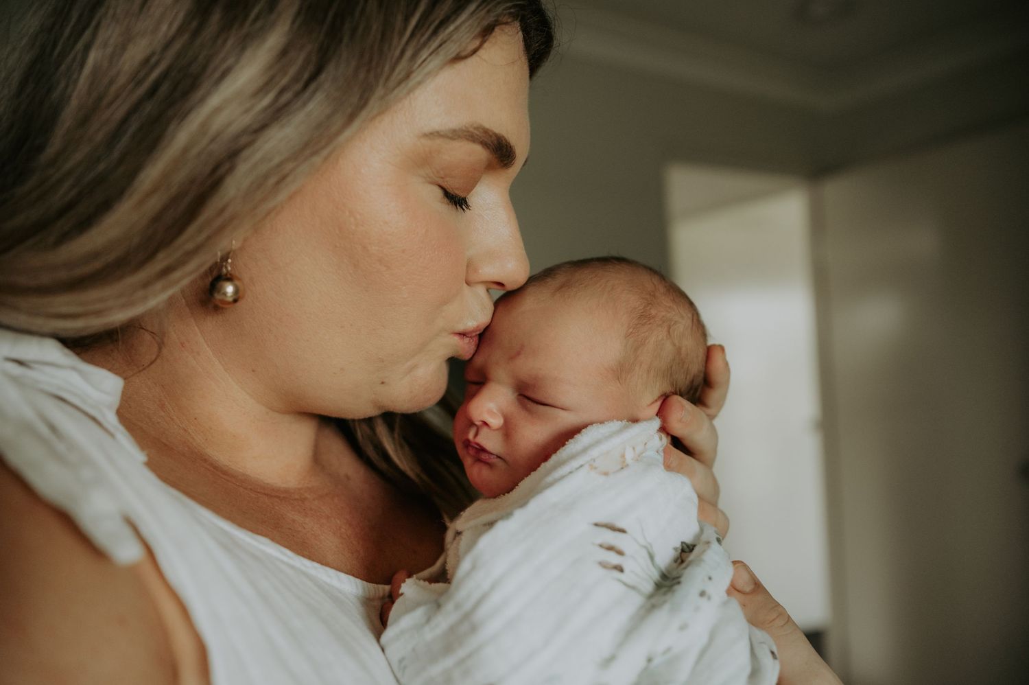 Tender moments captured between parent and newborn in soft, intimate indoor photography.
