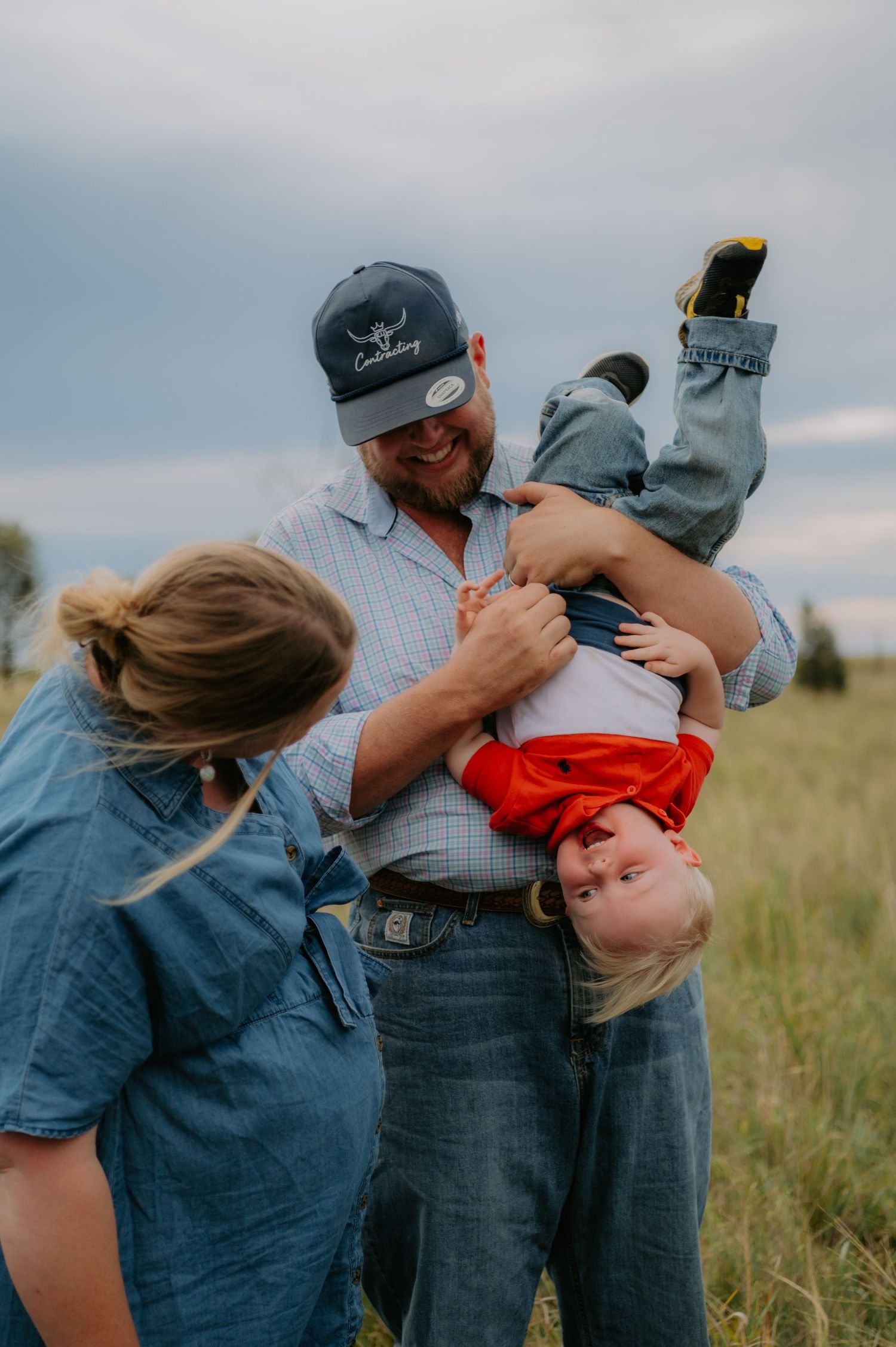 A playful family moment captured in a grassy field with denim outfits and joyful laughter.