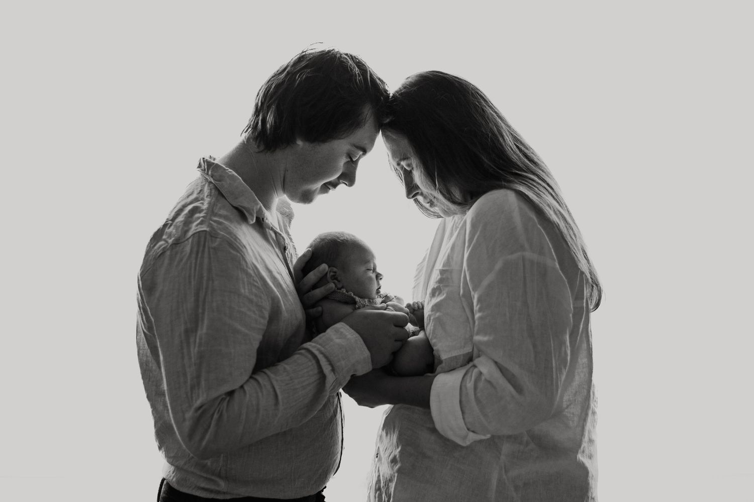 Black and white photo of new parents tenderly cradling their newborn baby together in a studio portrait.
