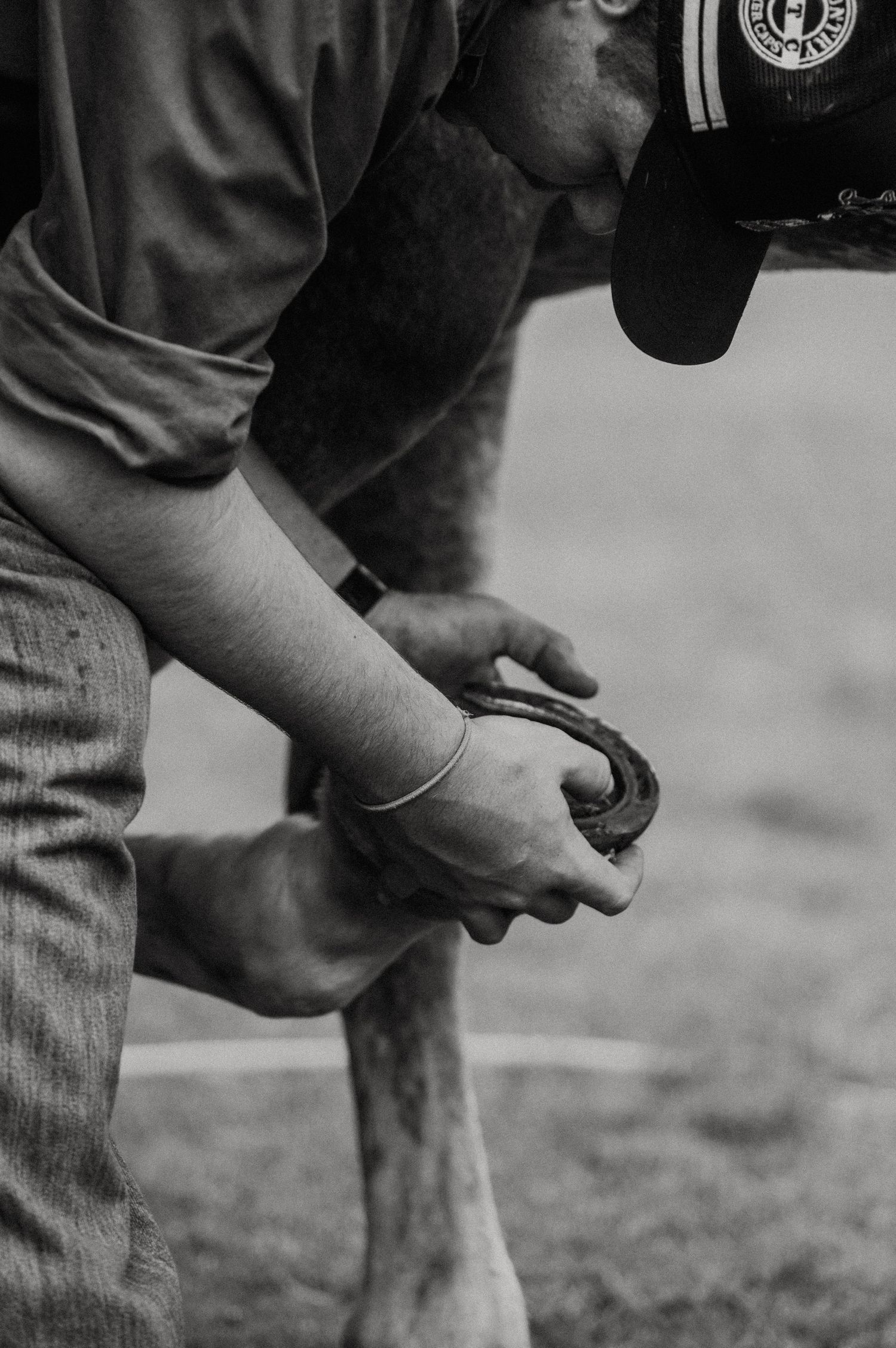Black and white photo of a farrier holding a horseshoe while working on a horse's hoof.