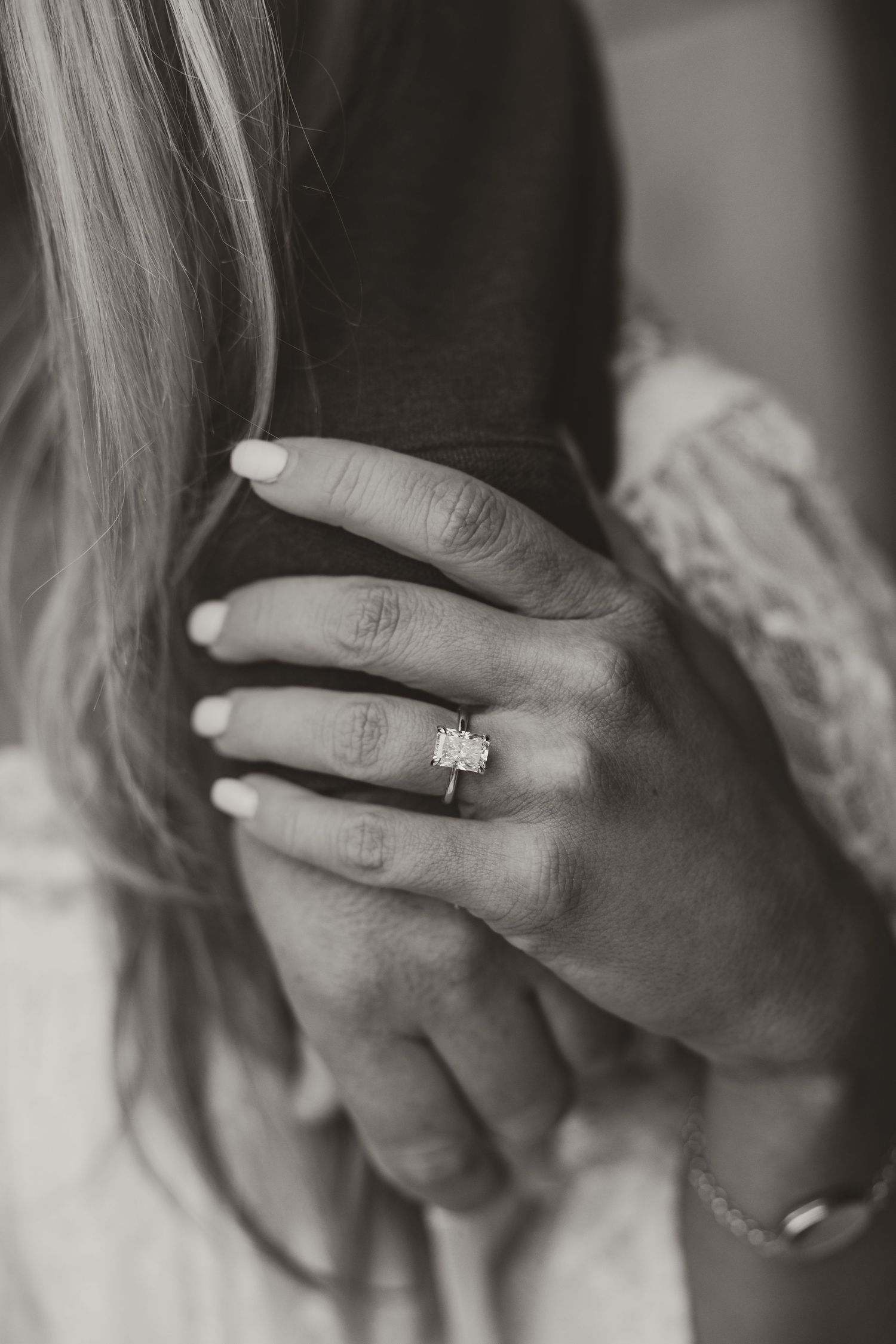 Black and white close-up photo of hands showing an engagement ring with a white stone.