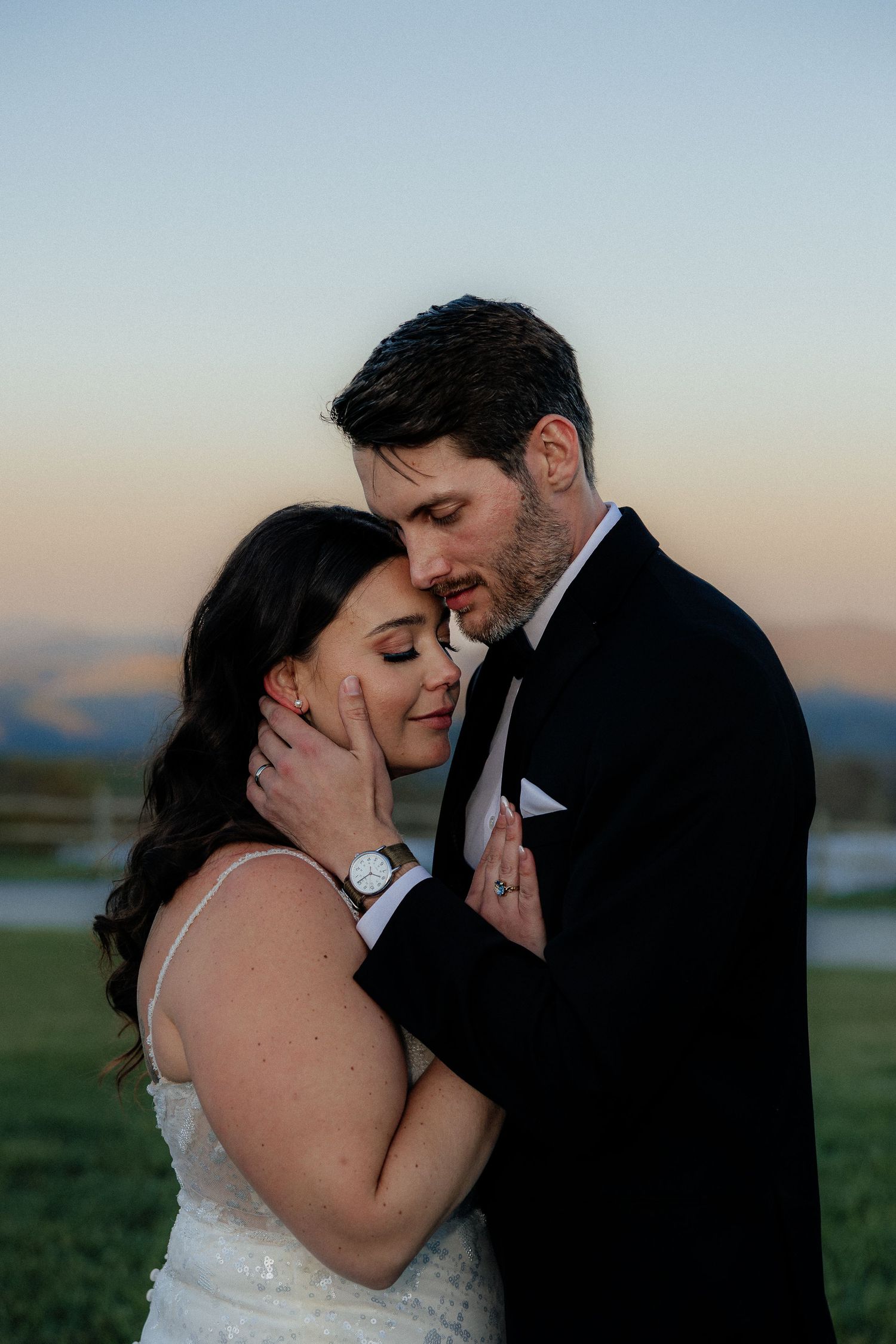 A bride and groom share an intimate embrace at sunset, with mountains in the background during their wedding portrait.