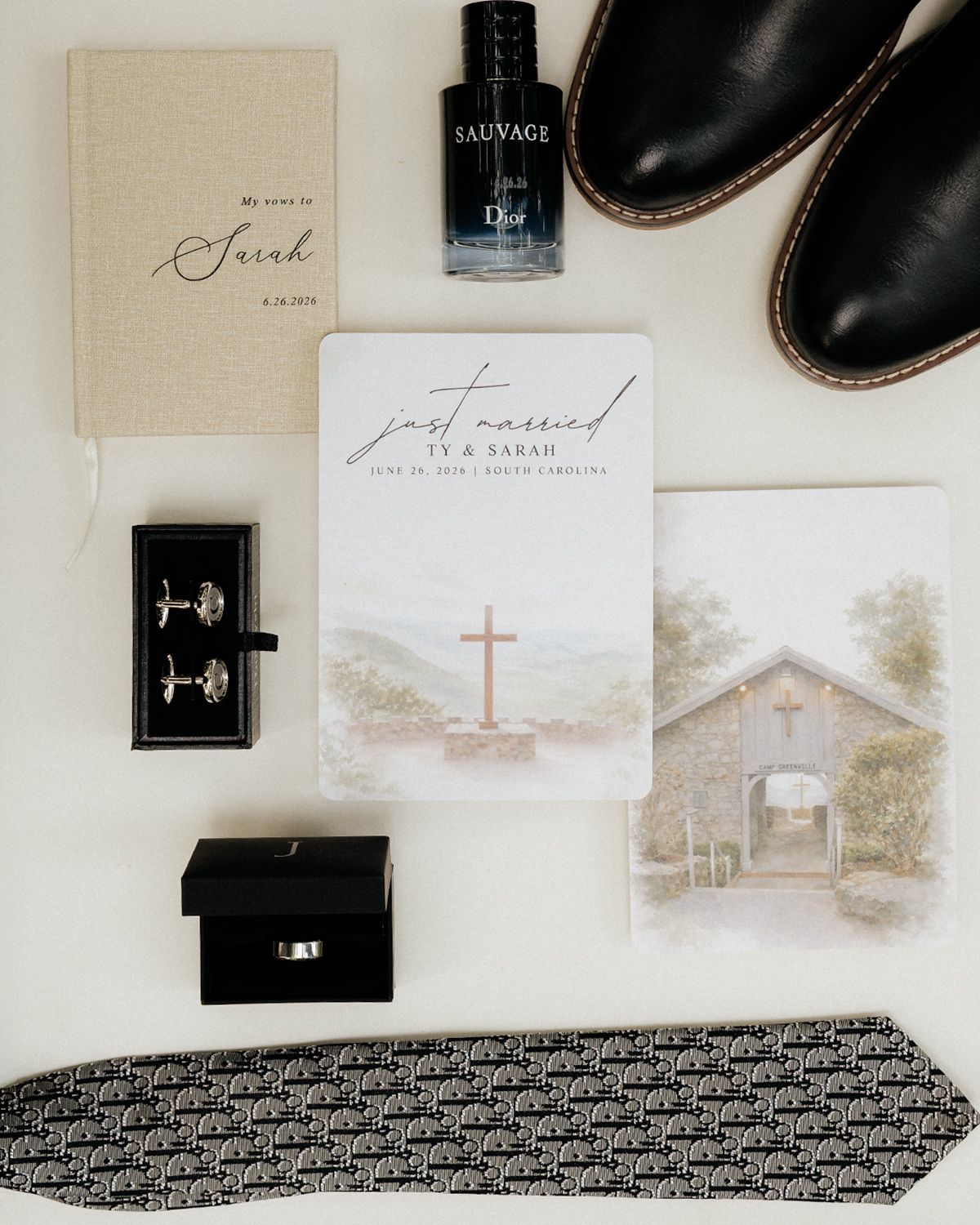 Elegant wedding flat lay with just married card, cufflinks, ring, patterned tie, Dior Sauvage cologne, and black dress shoes.