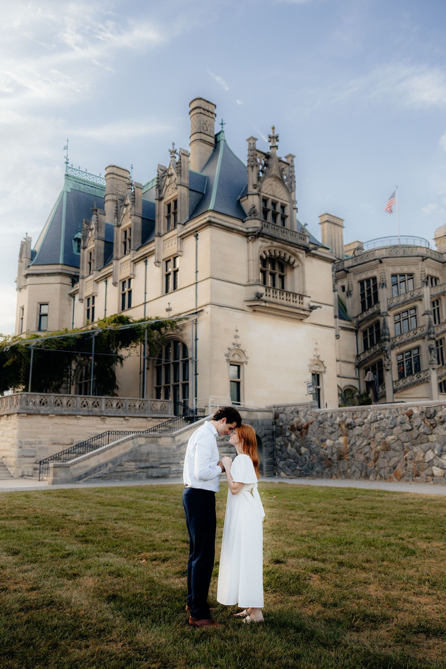 Couple embracing in front of the grand Biltmore Estate mansion in Asheville, NC, woman in white dress.