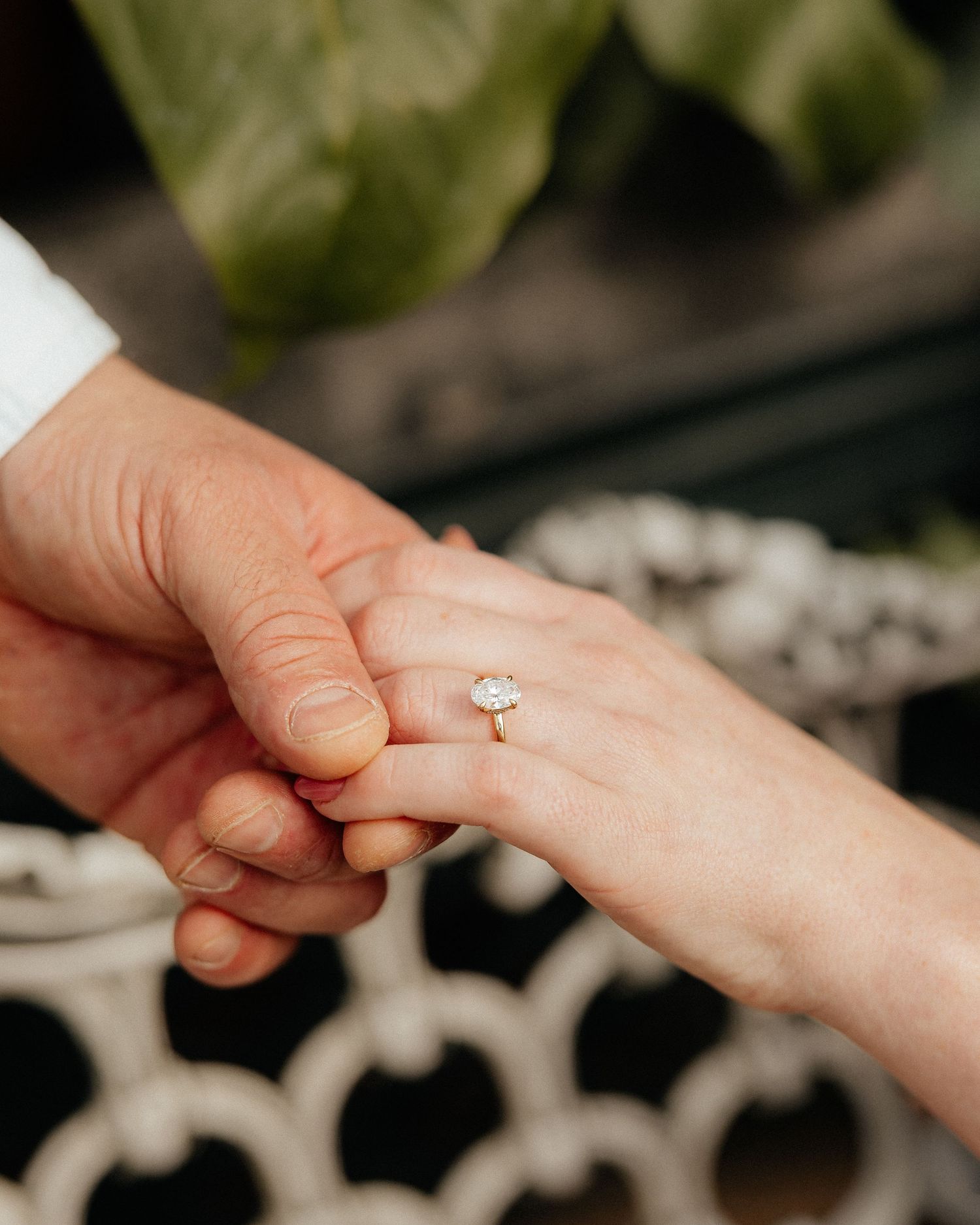 Close-up sequence of hands exchanging a diamond engagement ring in a romantic outdoor setting with white flowers.