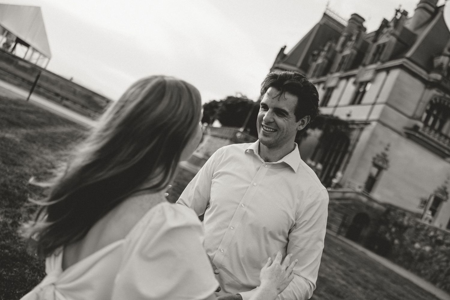 Black and white photo of a smiling couple sharing a romantic moment outside a grand estate building.