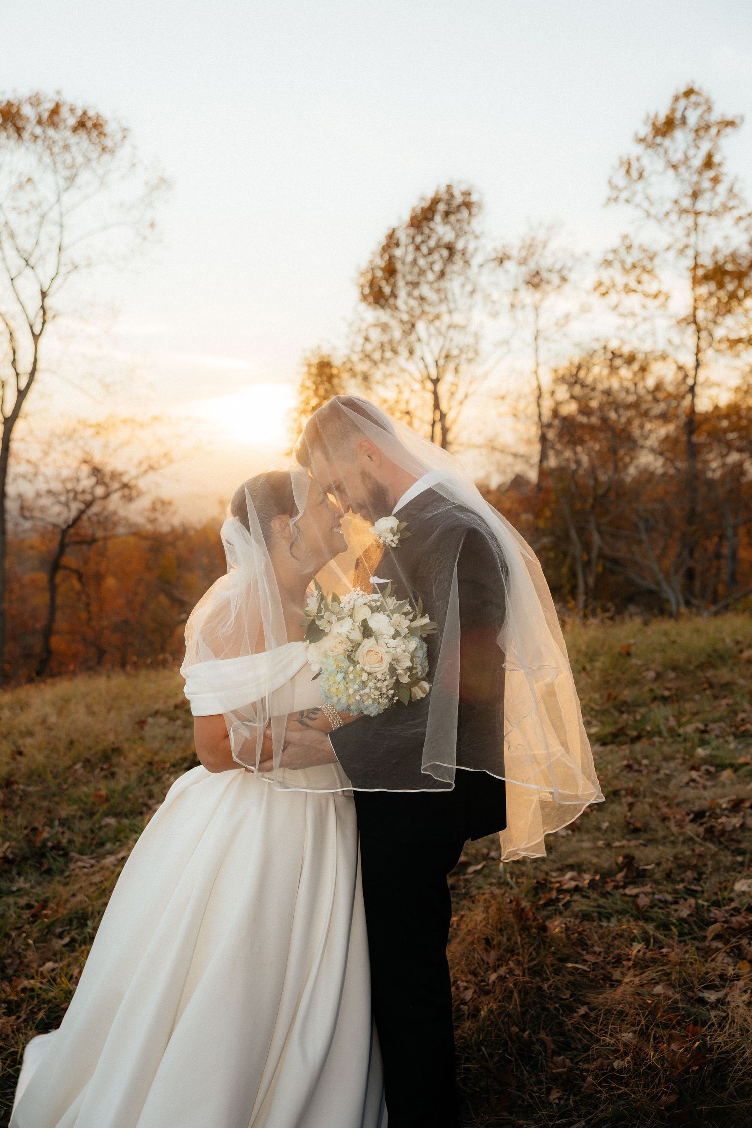 A romantic sunset wedding photo series shows a couple embracing under a flowing veil in an autumn field.