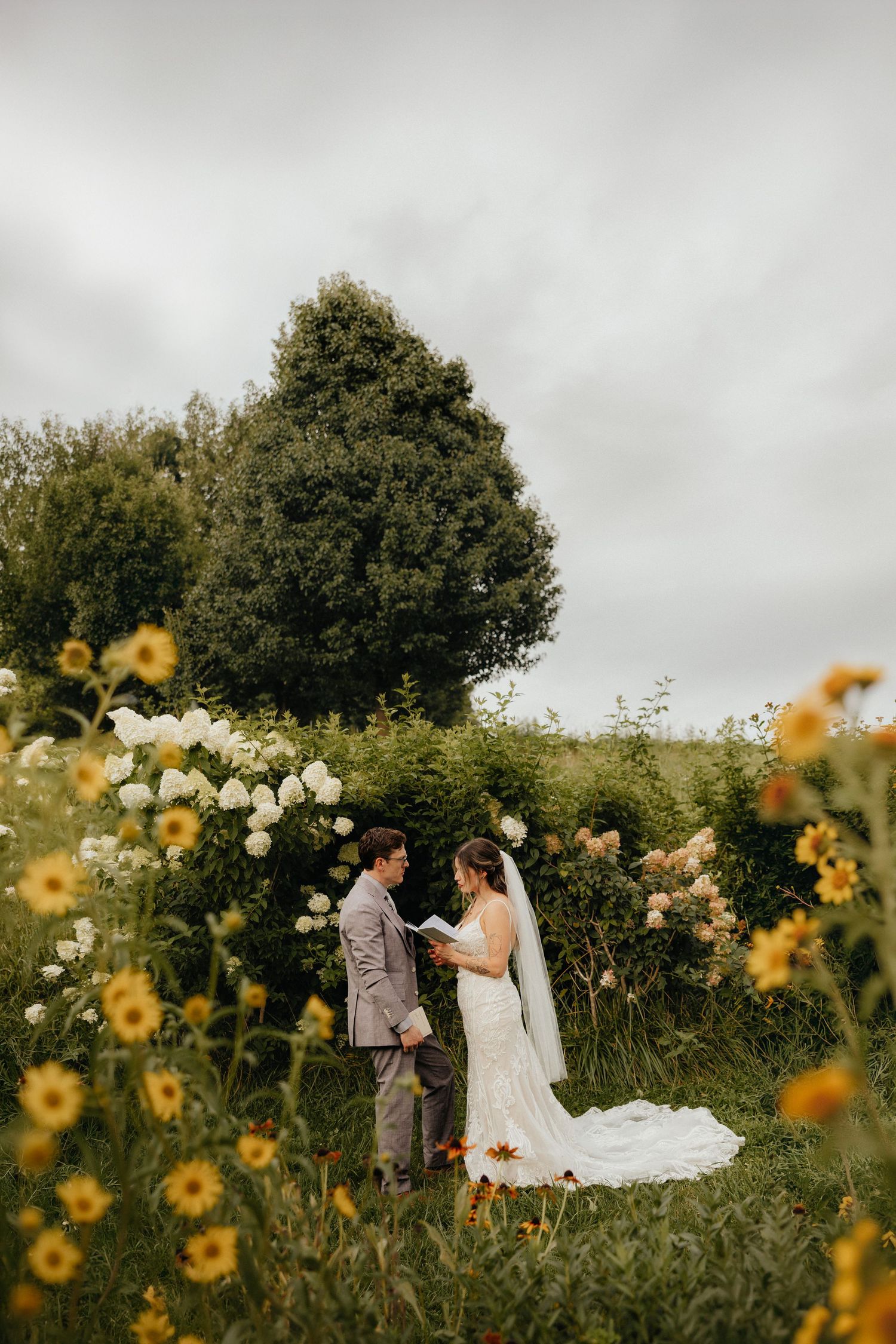 Bride and groom exchange vows surrounded by yellow wildflowers and white blooms in a lush garden setting.