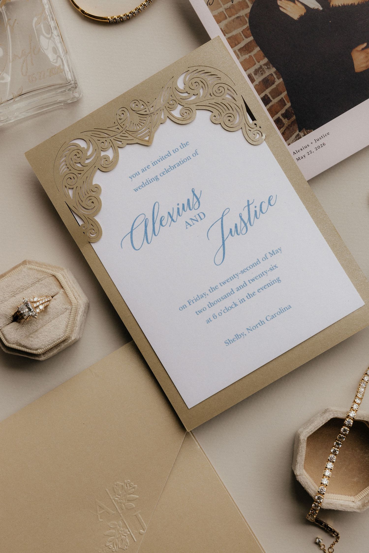 Elegant gold laser-cut wedding invitation for Alexius and Justice, styled with a diamond ring, bracelet, and envelope.