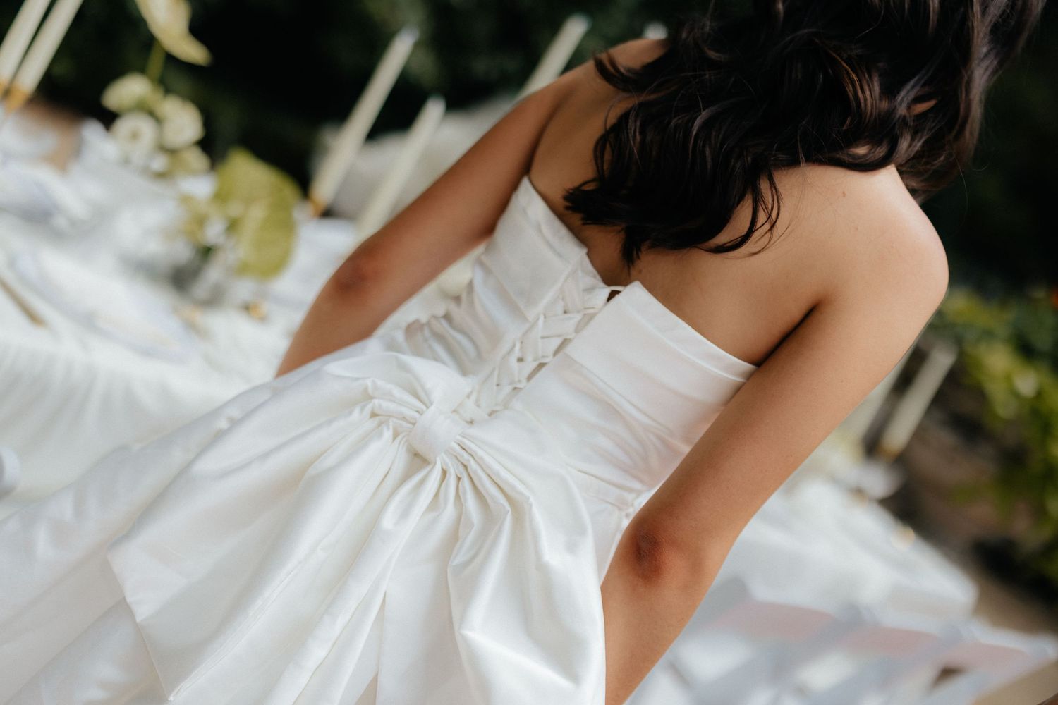 Bride in a stunning white strapless wedding gown with corset back detail, standing outdoors near elegant reception tables.