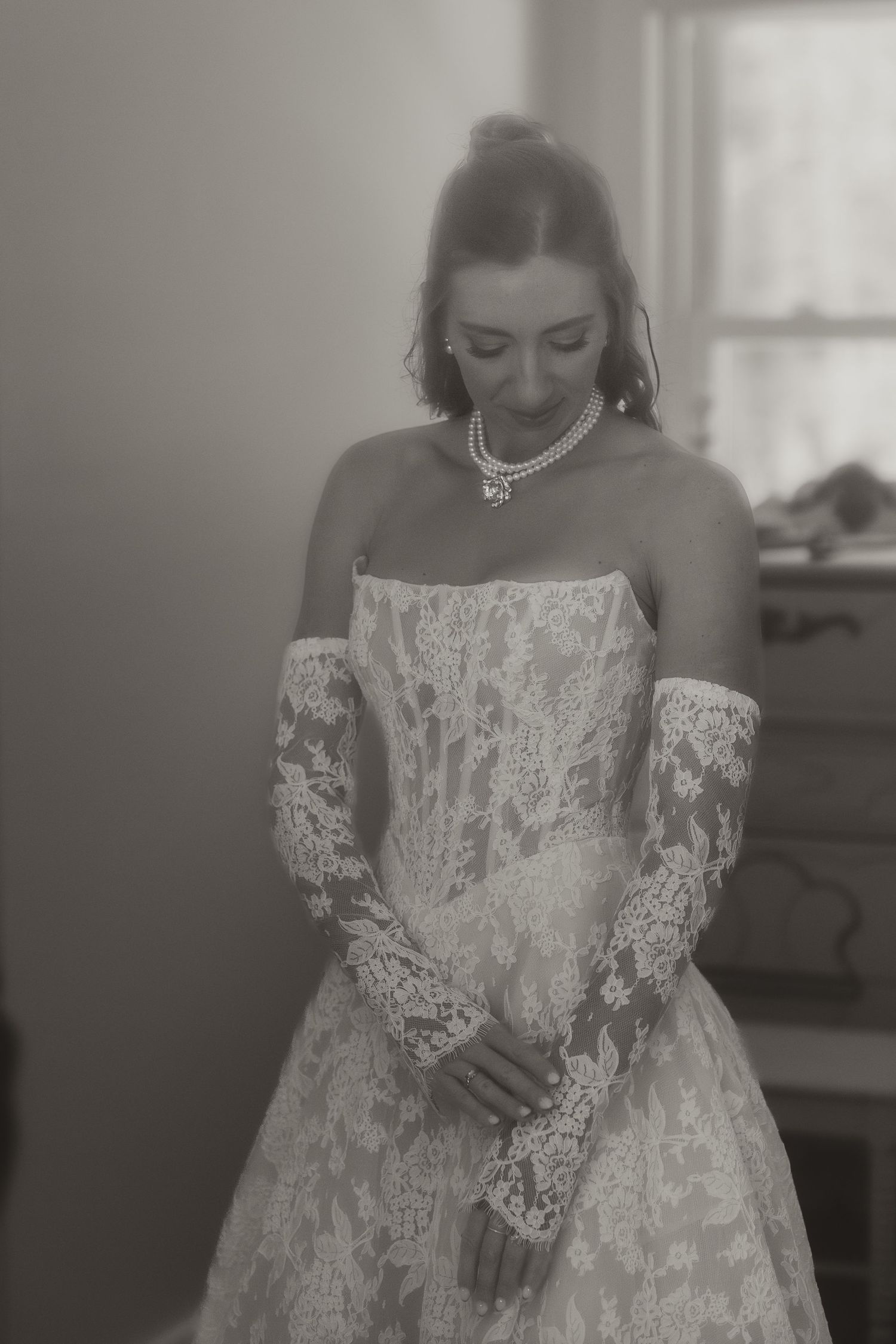 Black and white photo of a bride in a strapless lace wedding gown with long lace gloves and pearl necklace.