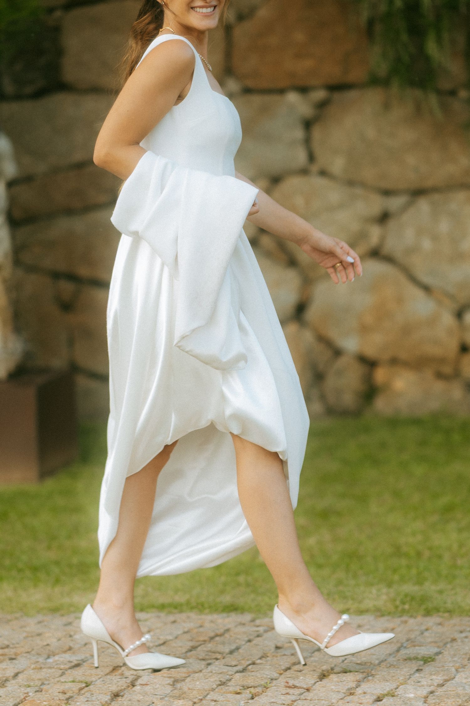 Bride walking in a sleek white high-low wedding dress with pearl heeled shoes on cobblestone.