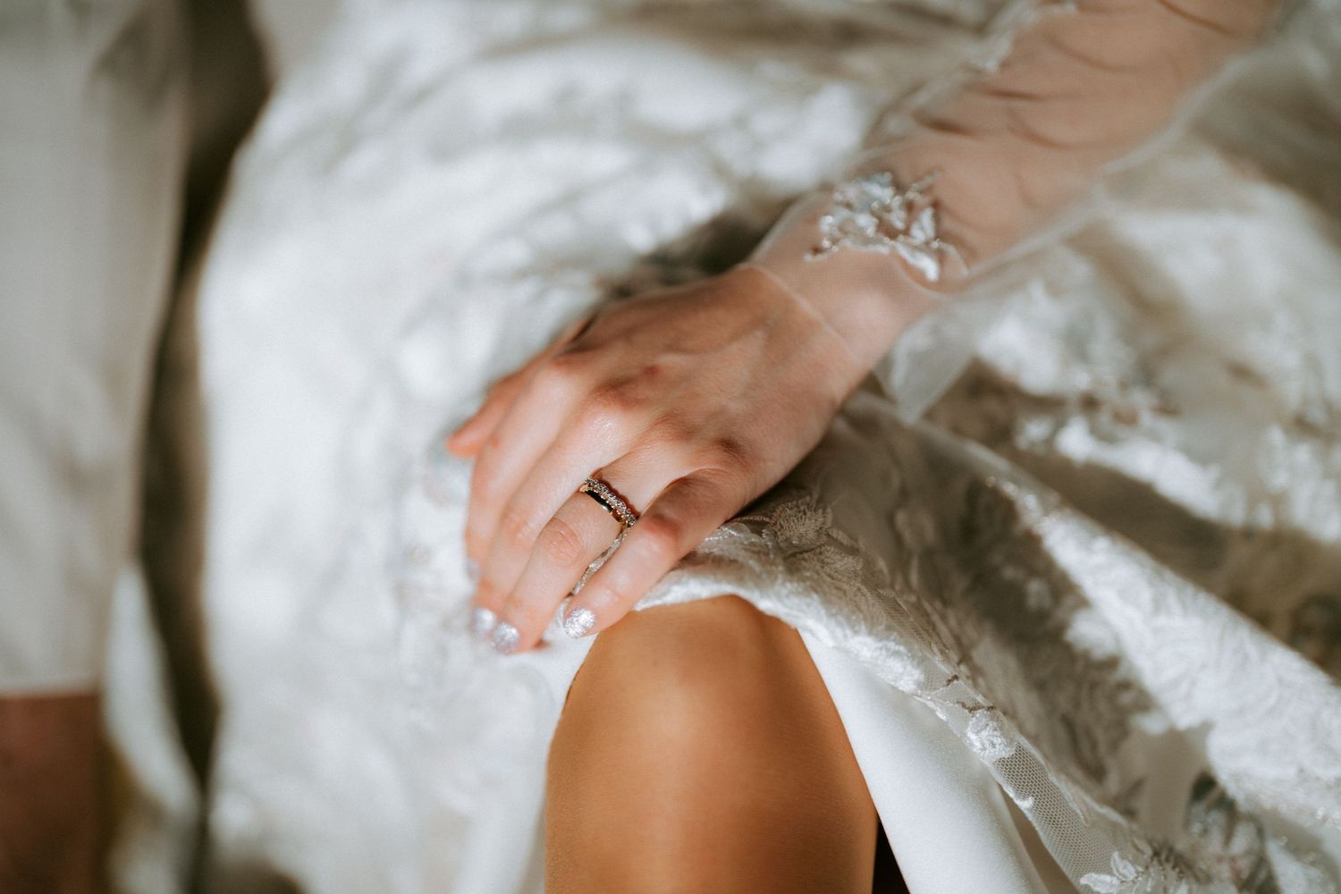 Close-up of bride's hand adorned with delicate gold rings resting on her lace wedding dress.