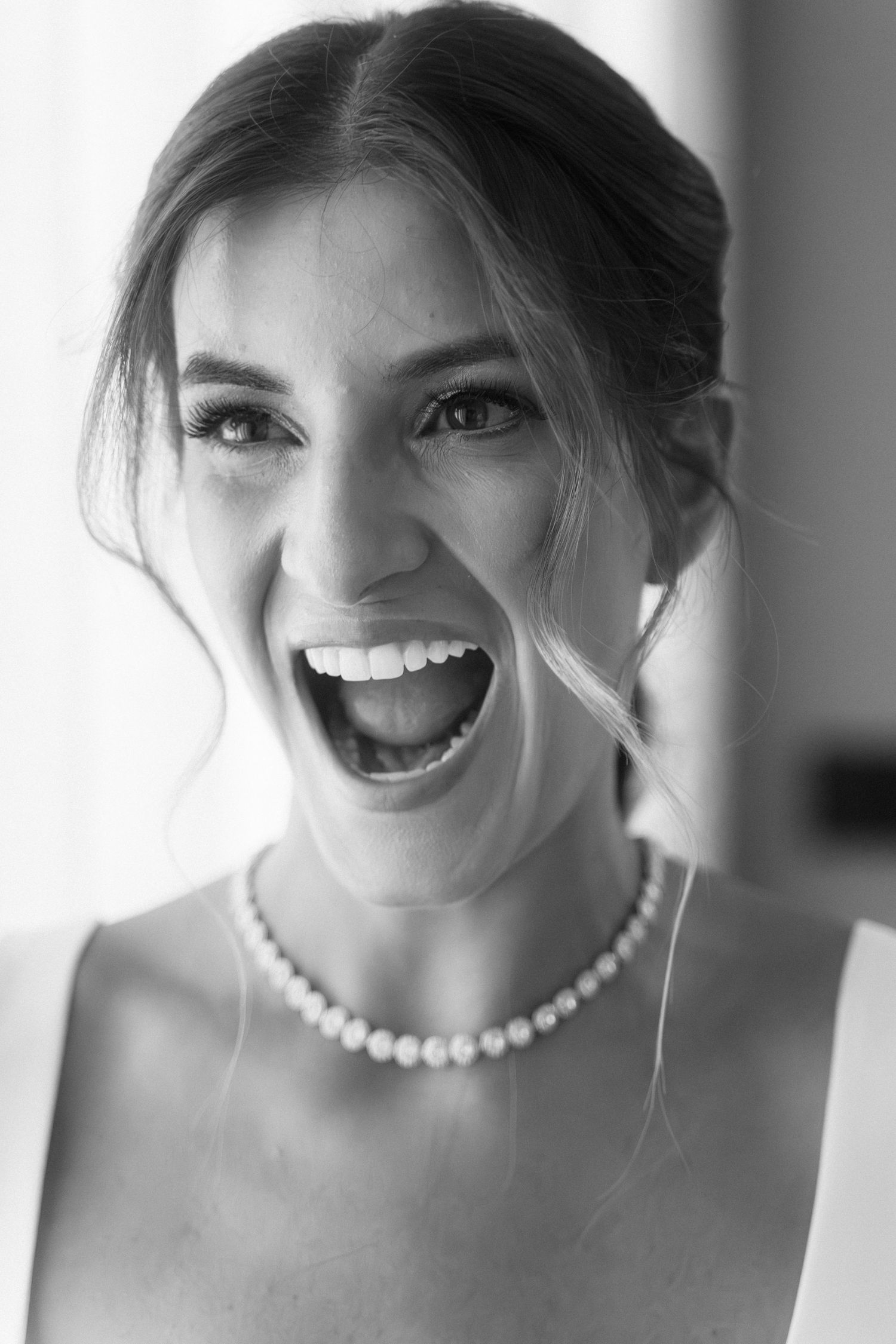 Black and white portrait of joyful bride laughing wearing pearl necklace on wedding day.
