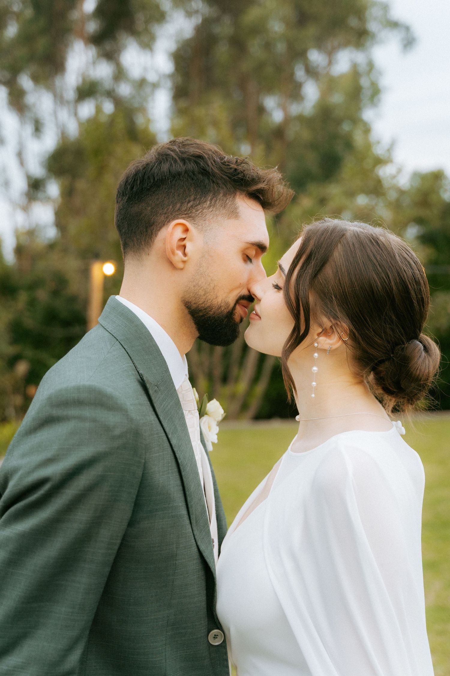 Bride and groom share an intimate moment outdoors, nearly kissing in a lush green garden setting.