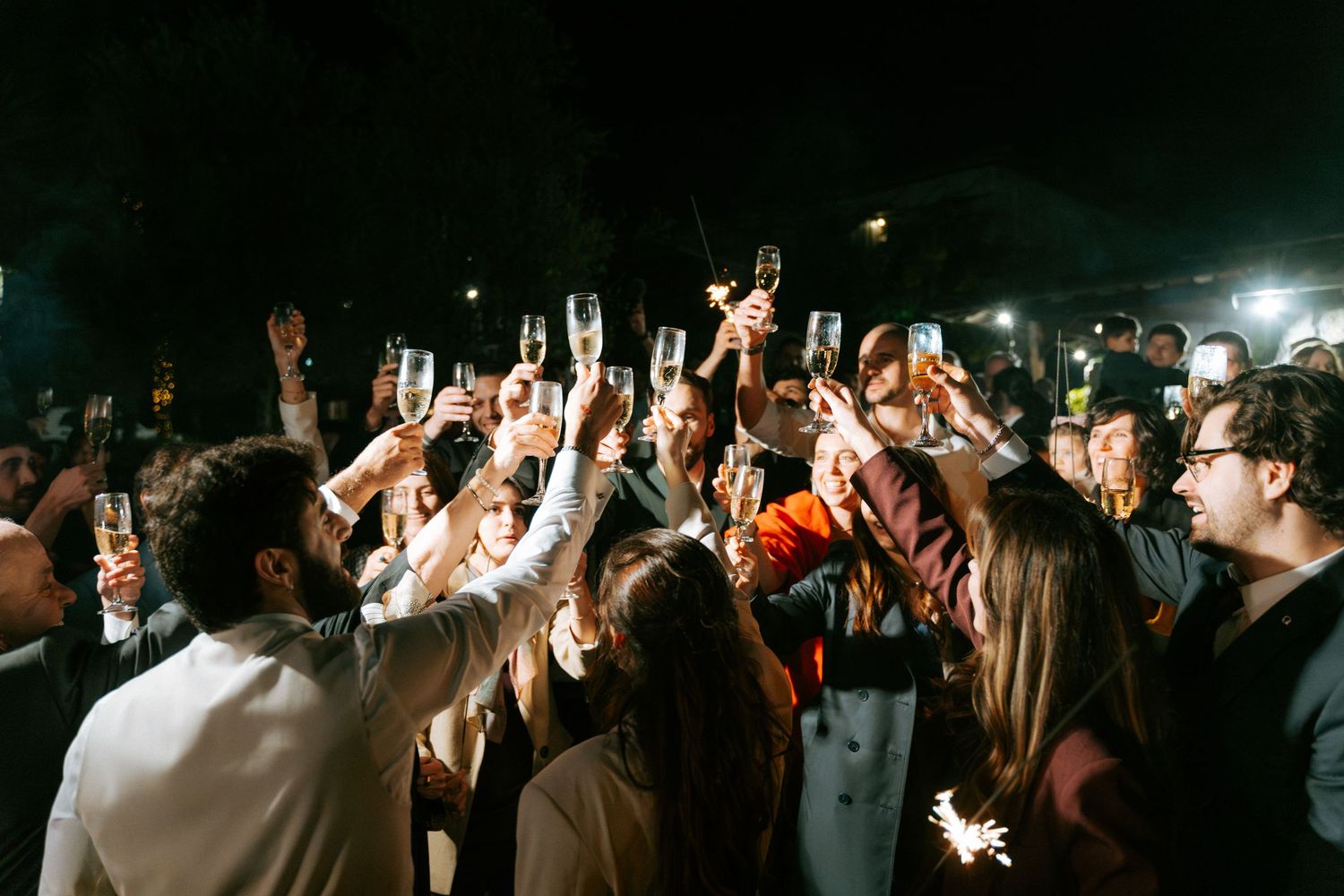 Guests raising champagne glasses in a celebratory toast at a nighttime wedding reception.