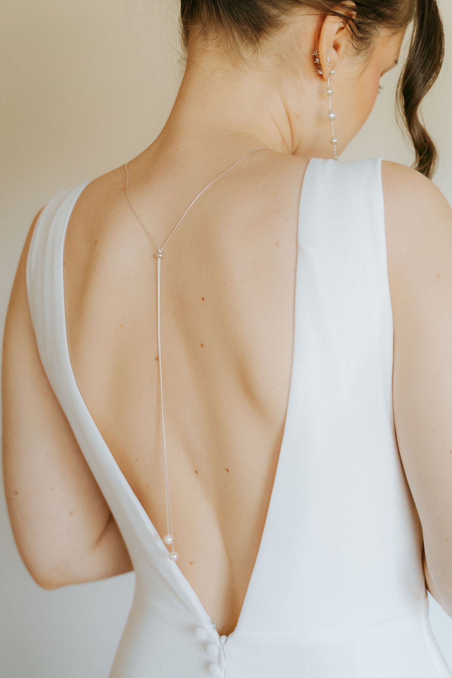 Close-up of bride's open back wedding dress with delicate pearl and chain back necklace detail.