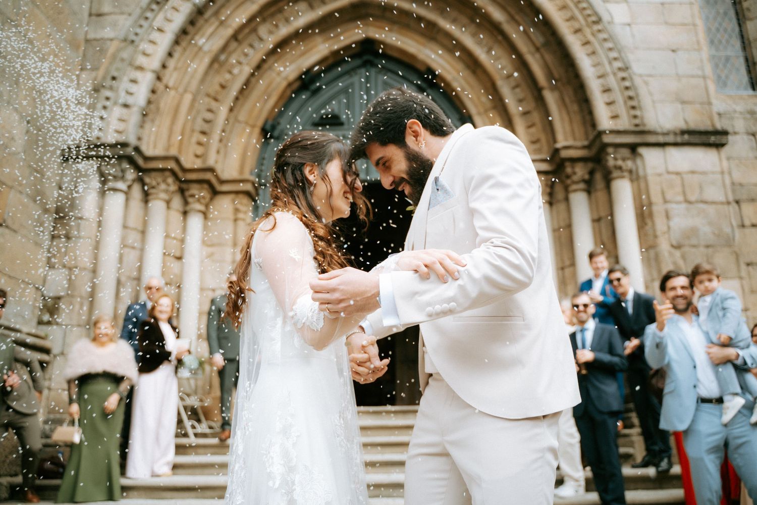 Newlyweds share a joyful moment as confetti falls outside a historic stone church after ceremony.