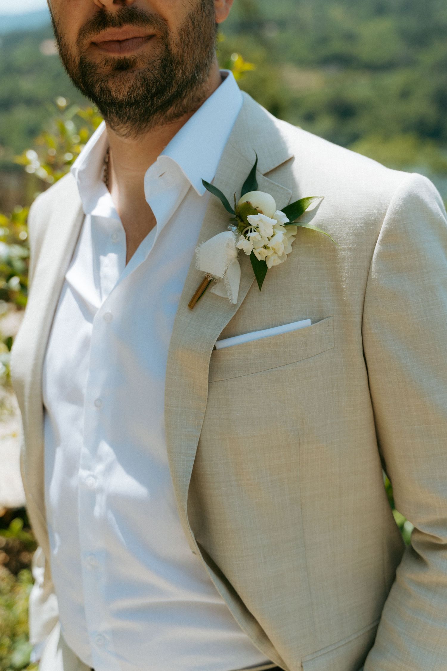 Close-up of groom's beige wedding suit with white floral boutonniere and pocket square.