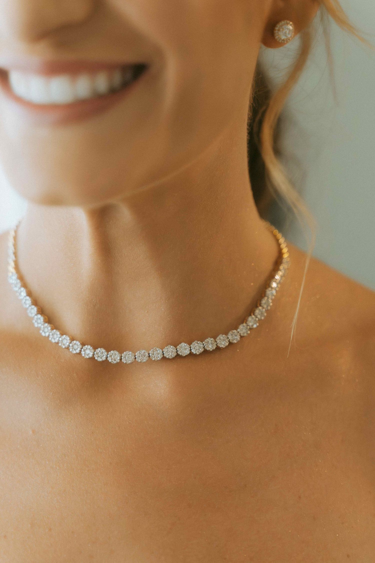Close-up of a smiling bride wearing an elegant diamond tennis choker necklace and stud earrings.