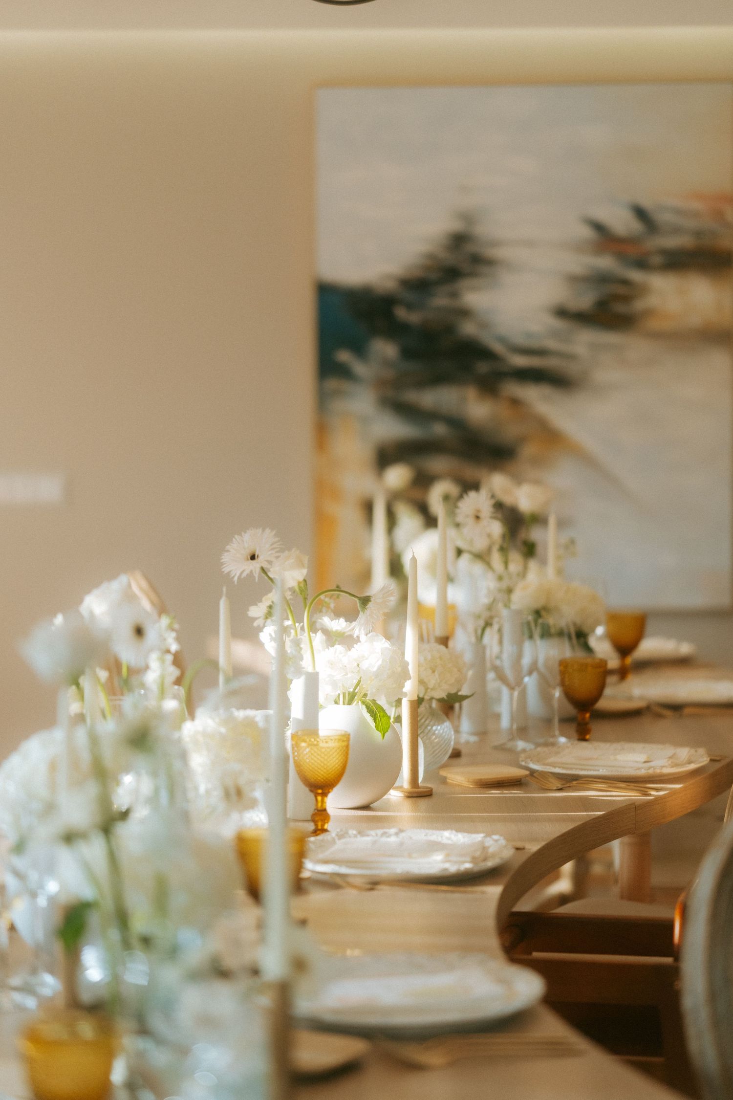 Elegant wedding reception table with white floral arrangements, amber goblets, and candles on a wooden table.