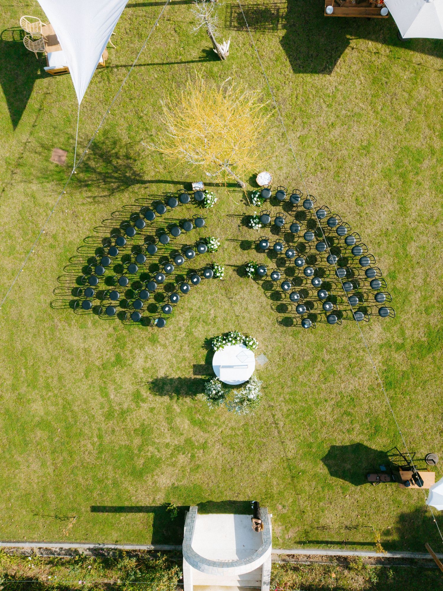 Aerial drone view of curved wedding ceremony chairs arranged in semicircle on green lawn.