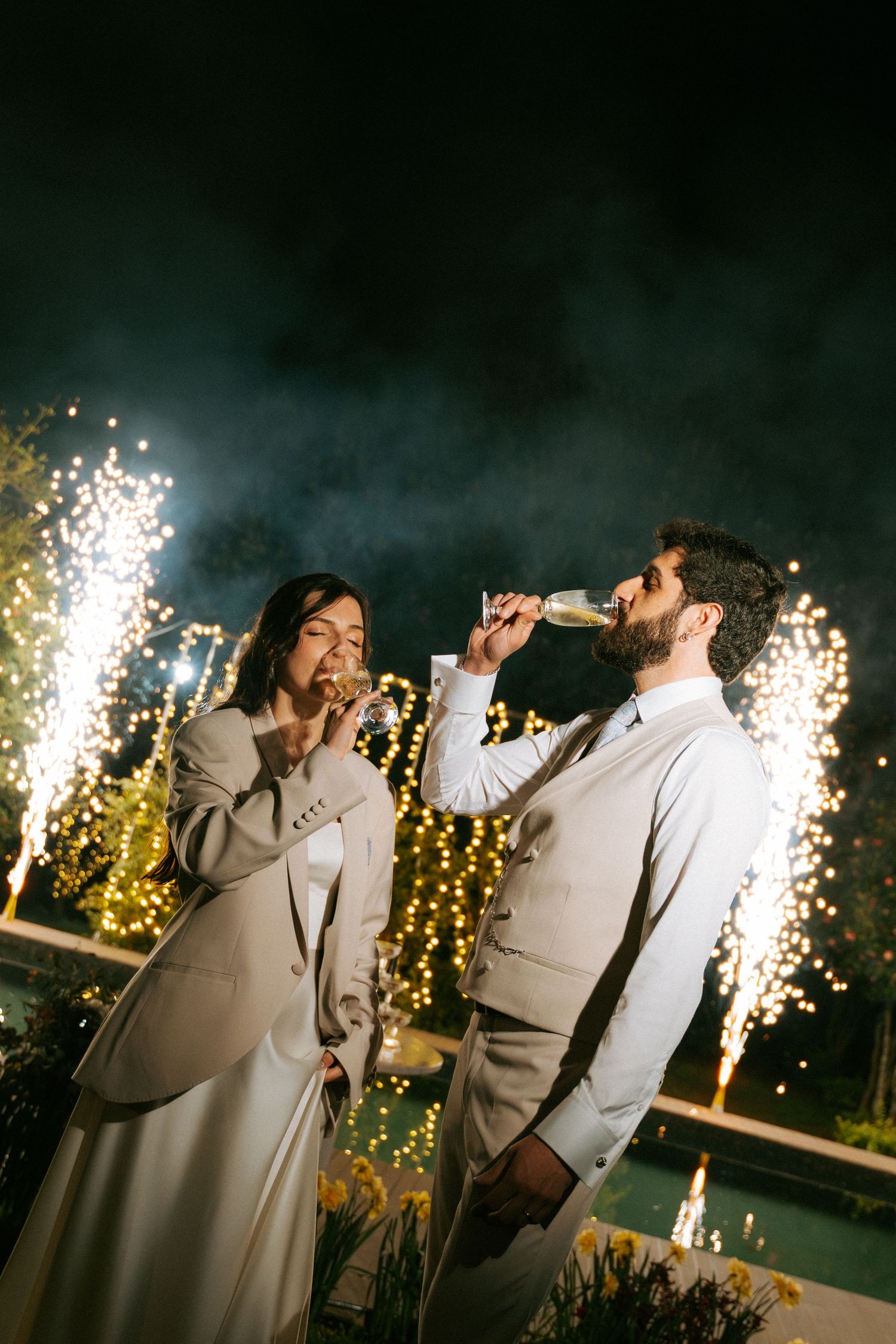 Newlyweds toast champagne together surrounded by spectacular fireworks display at night celebration.