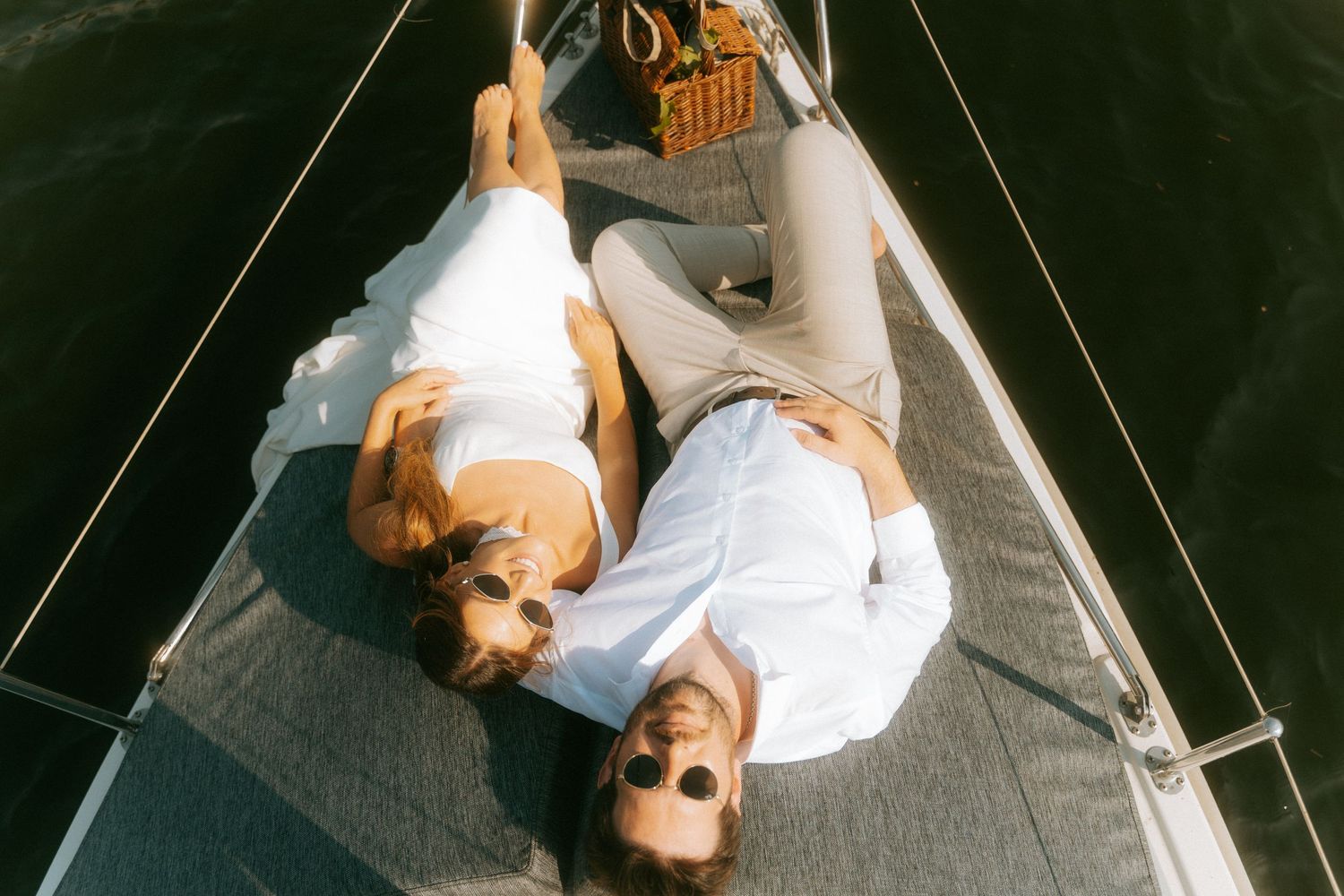 Aerial view of a bride and groom relaxing on the bow of a sailboat on calm water.