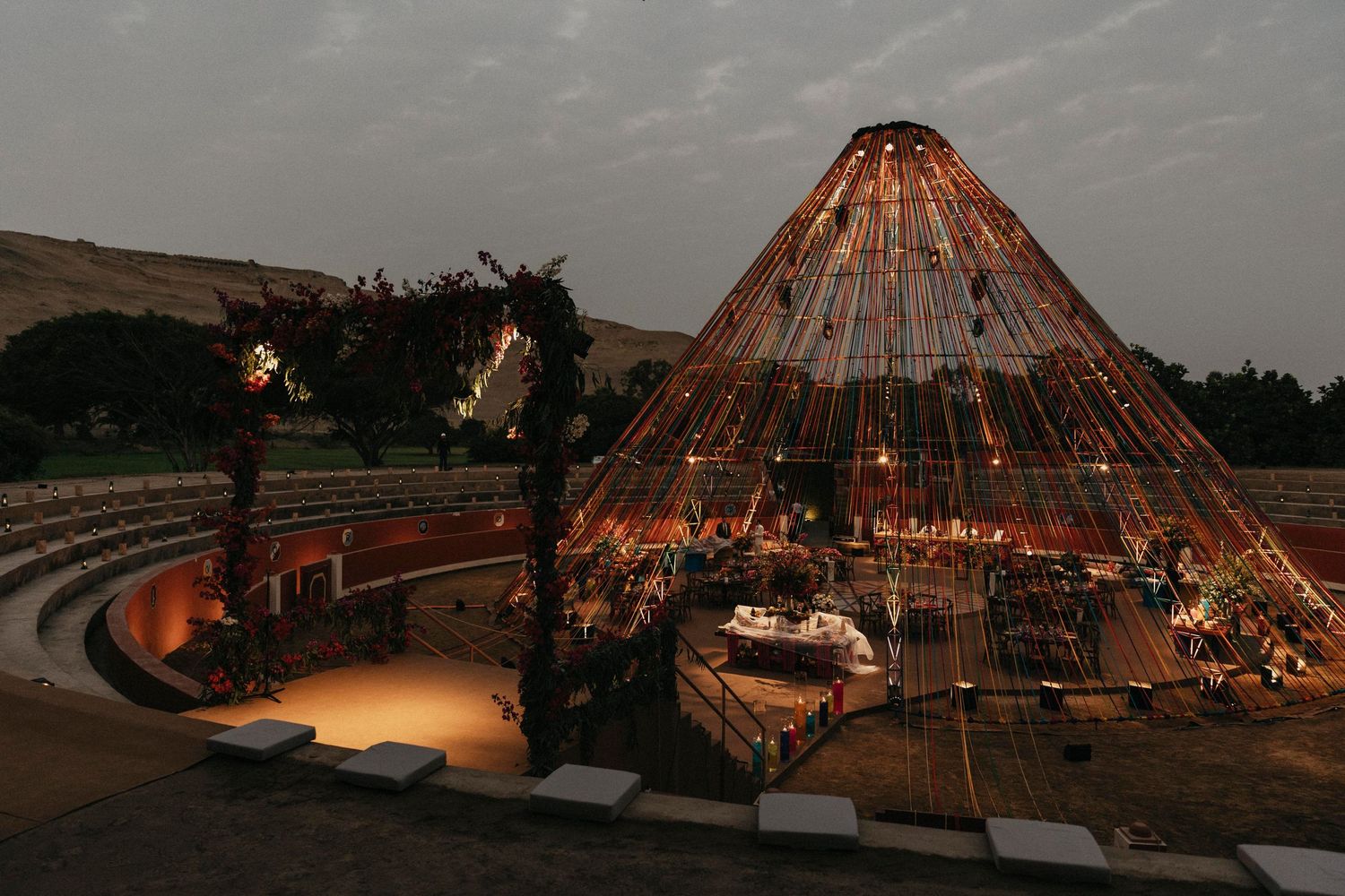 Stunning pyramid-shaped wedding venue with string lights glows at dusk in an open-air amphitheater setting.